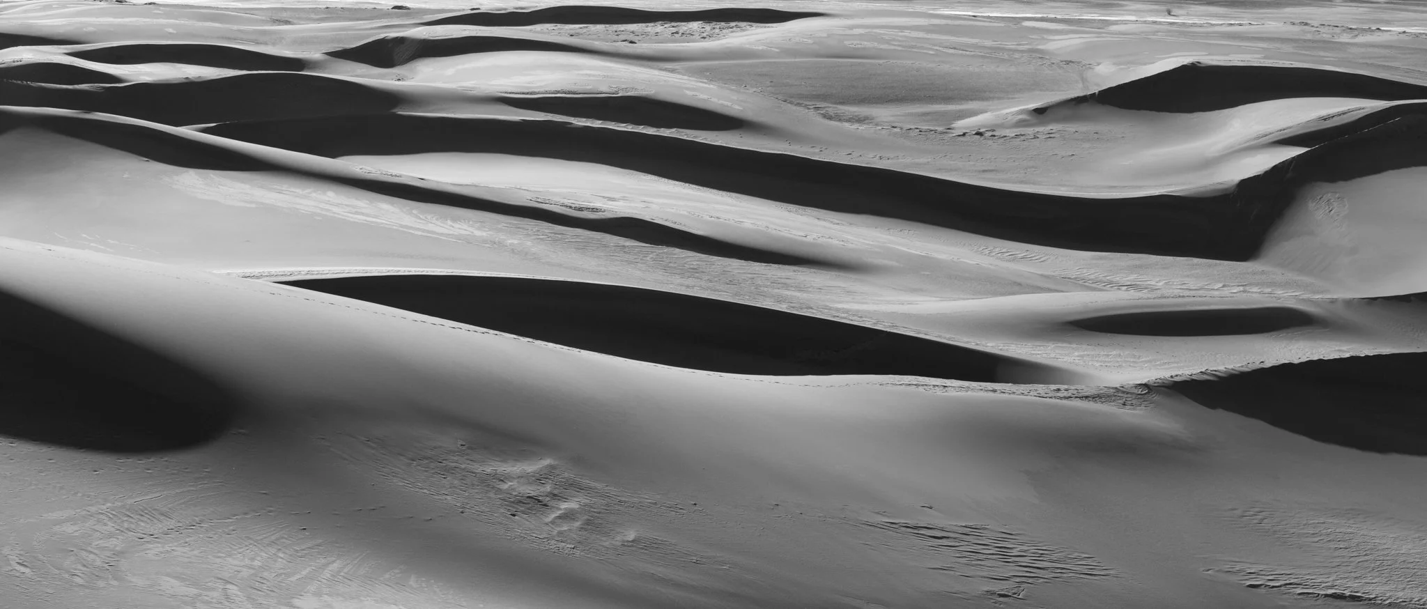 panoramic black and white image of sand dunes with harsh shadows
