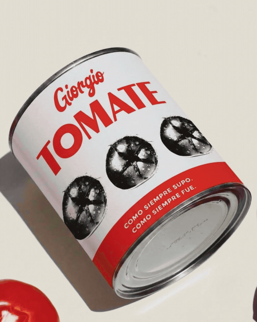 Lata de tomate de la marca Giorgio, con la etiqueta en blanco y negro, y la palabra 'TOMATE' en letras rojas. La etiqueta también tiene imágenes en blanco y negro de tomates, con la frase en español 'Como siempre supo. Como siempre fue.'