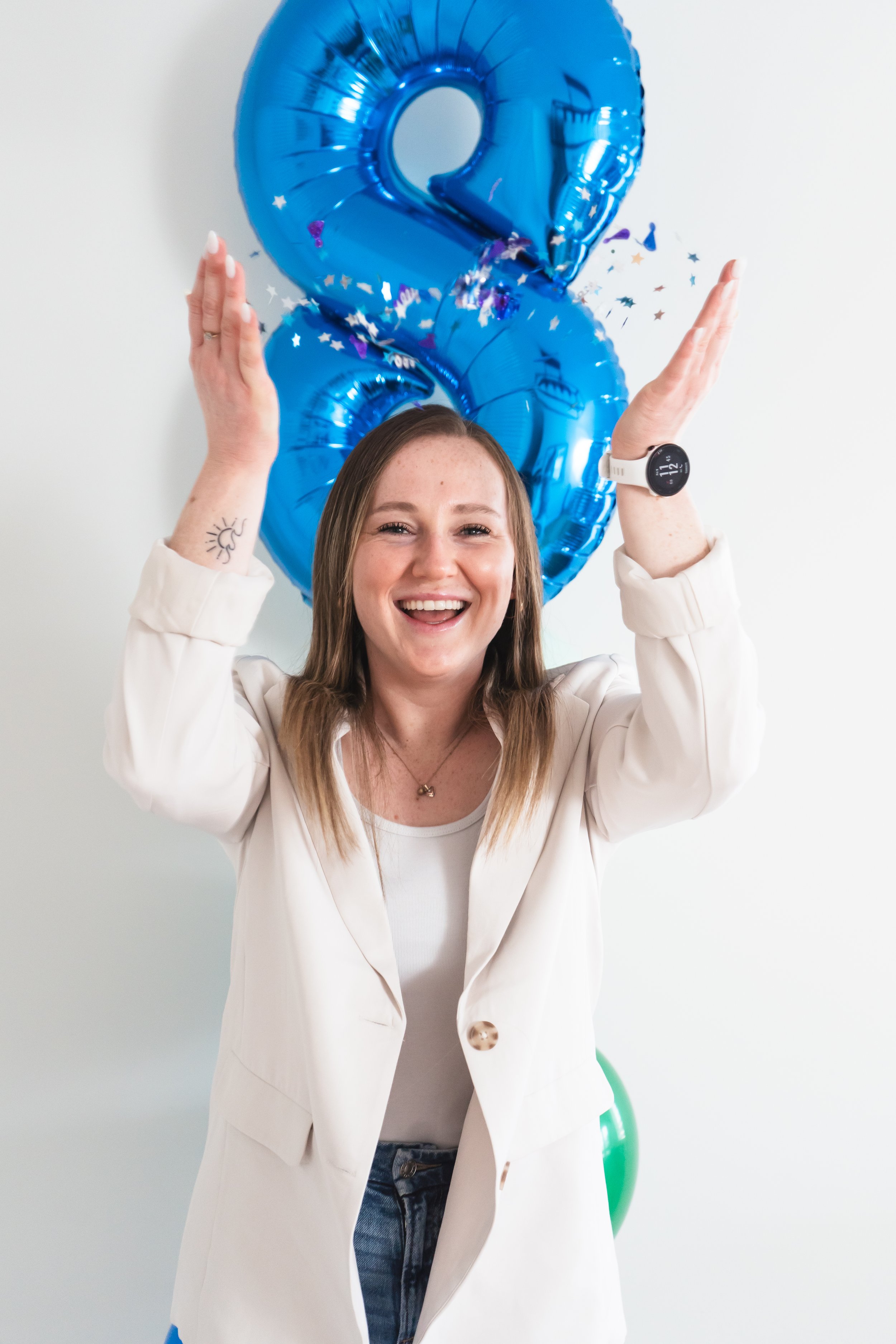 A personal fitness coach from Brantford Ontario Canada throwing confetti in the air, smiling at the camera, a balloon 8 behind her.