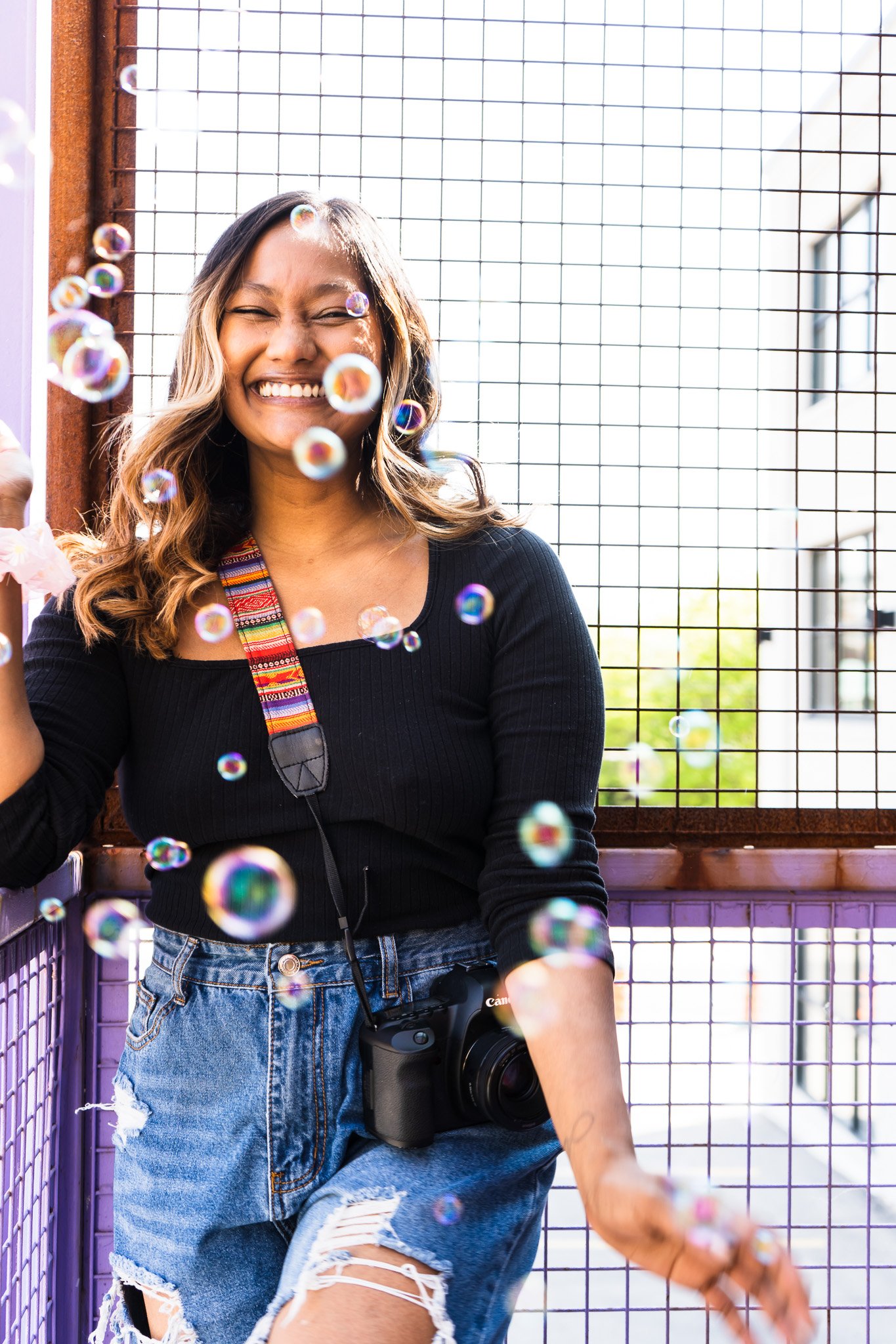 A photographer from Kitchener Ontario Canada posing in front of a gate smiling confidently, bubbles are floating in the foreground.