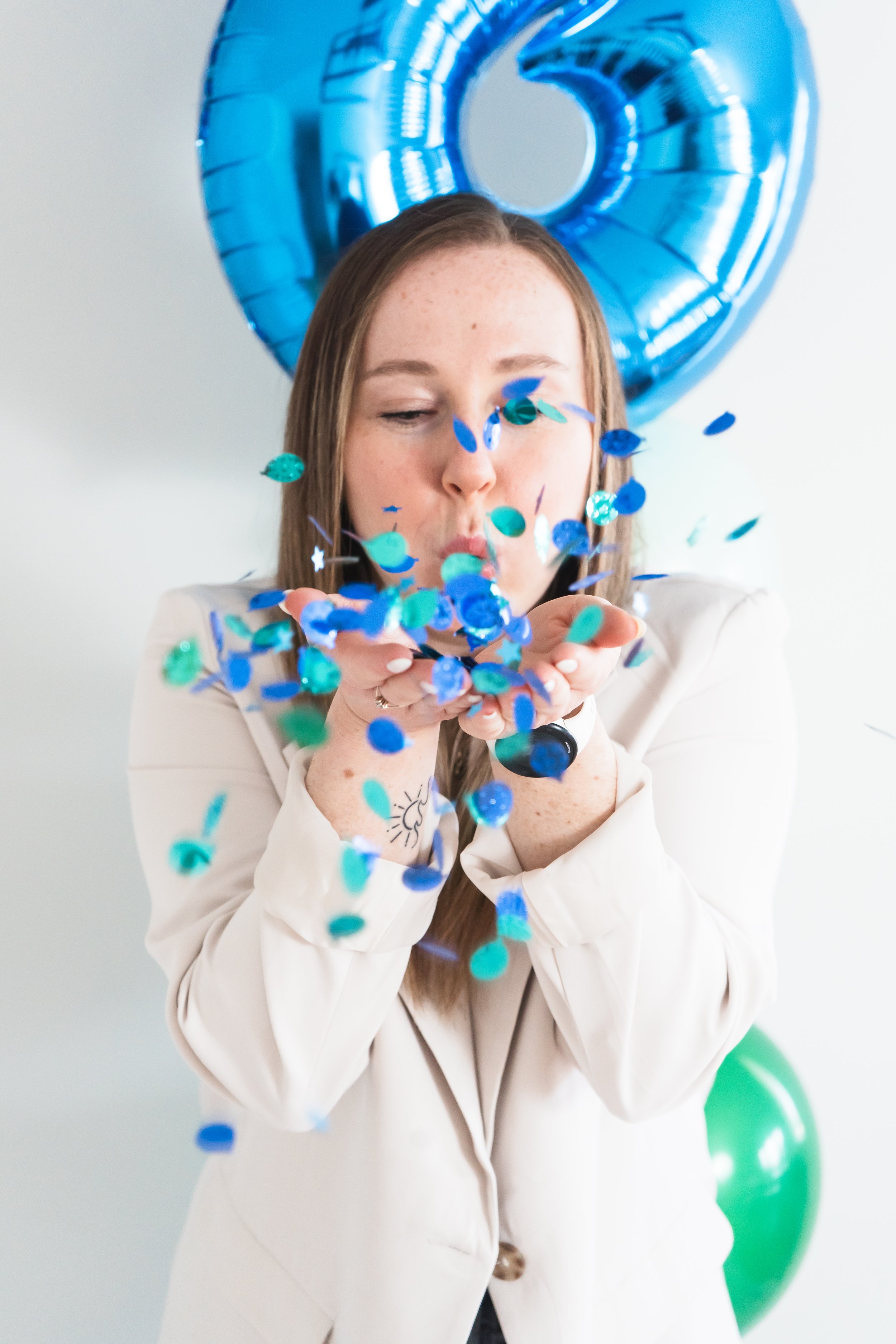 A fitness coach from Brantford Ontario blowing blue and green confetti towards the camera of a brand photographer.