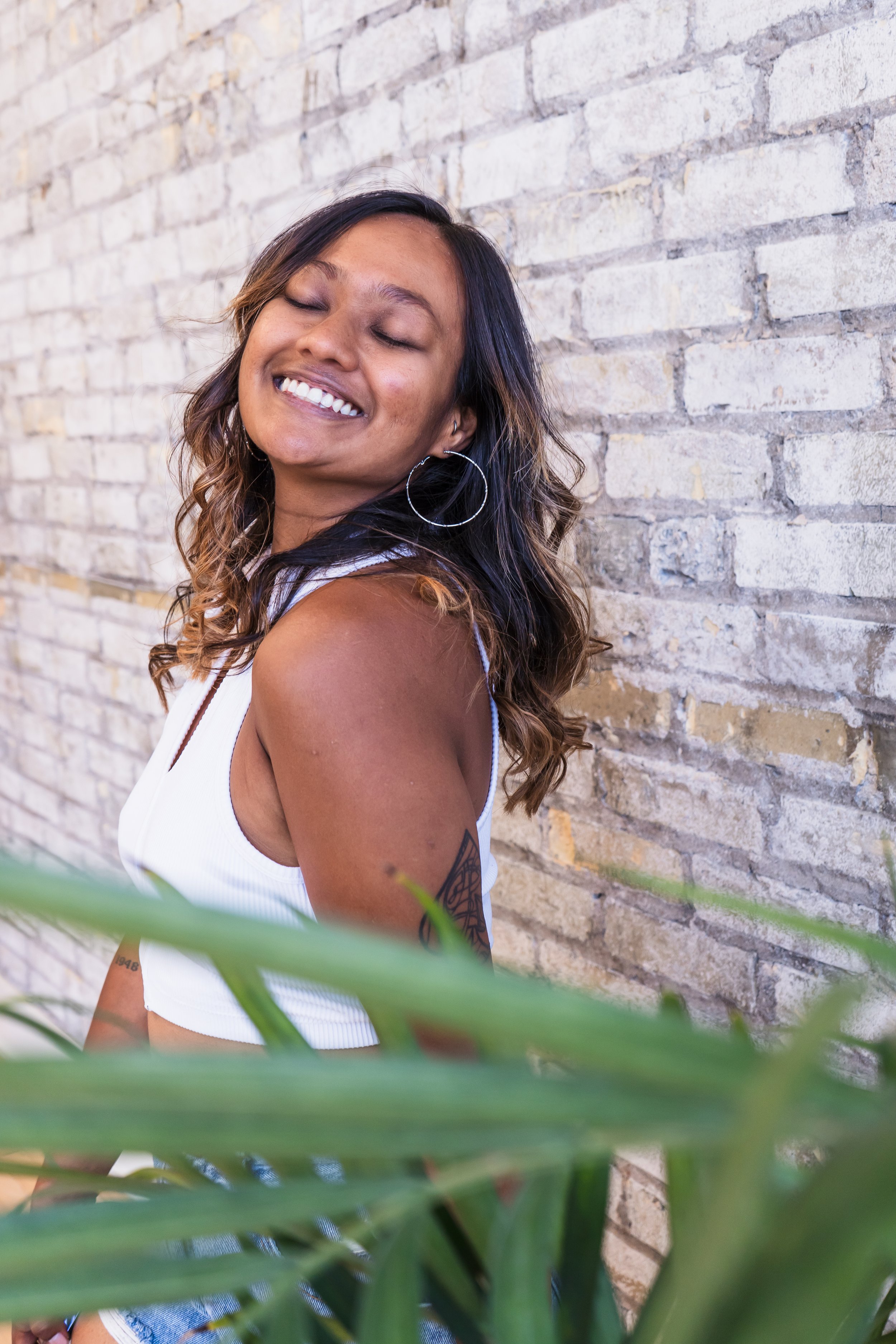 A photographer from Kitchener Ontario Canada smiling confidently at the camera, a plant in the foreground and a brick wall behind her.