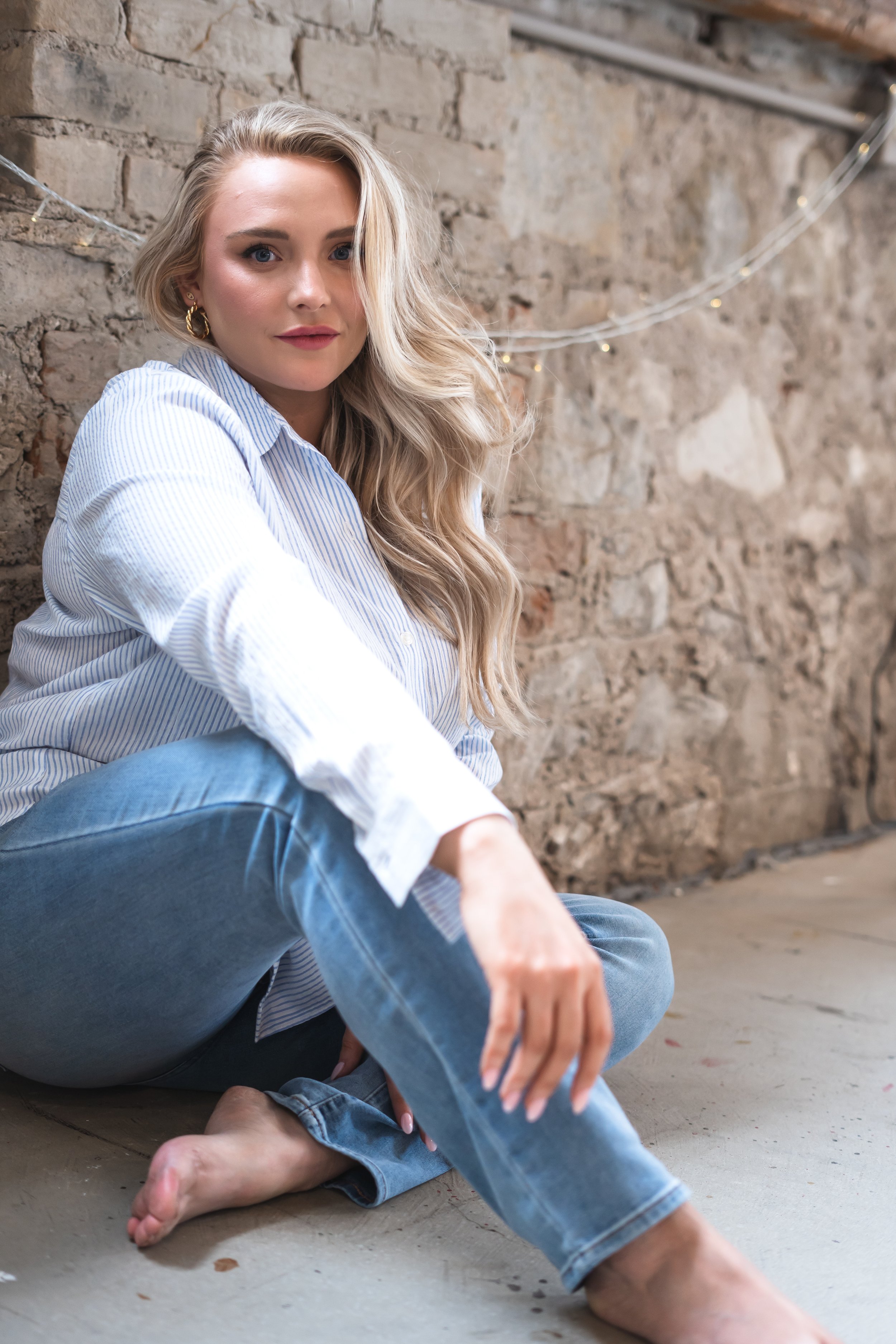 A real estate agent from Hamilton Ontario Canada posing on the floor in front of a stone wall with her hair falling slightly over her face.