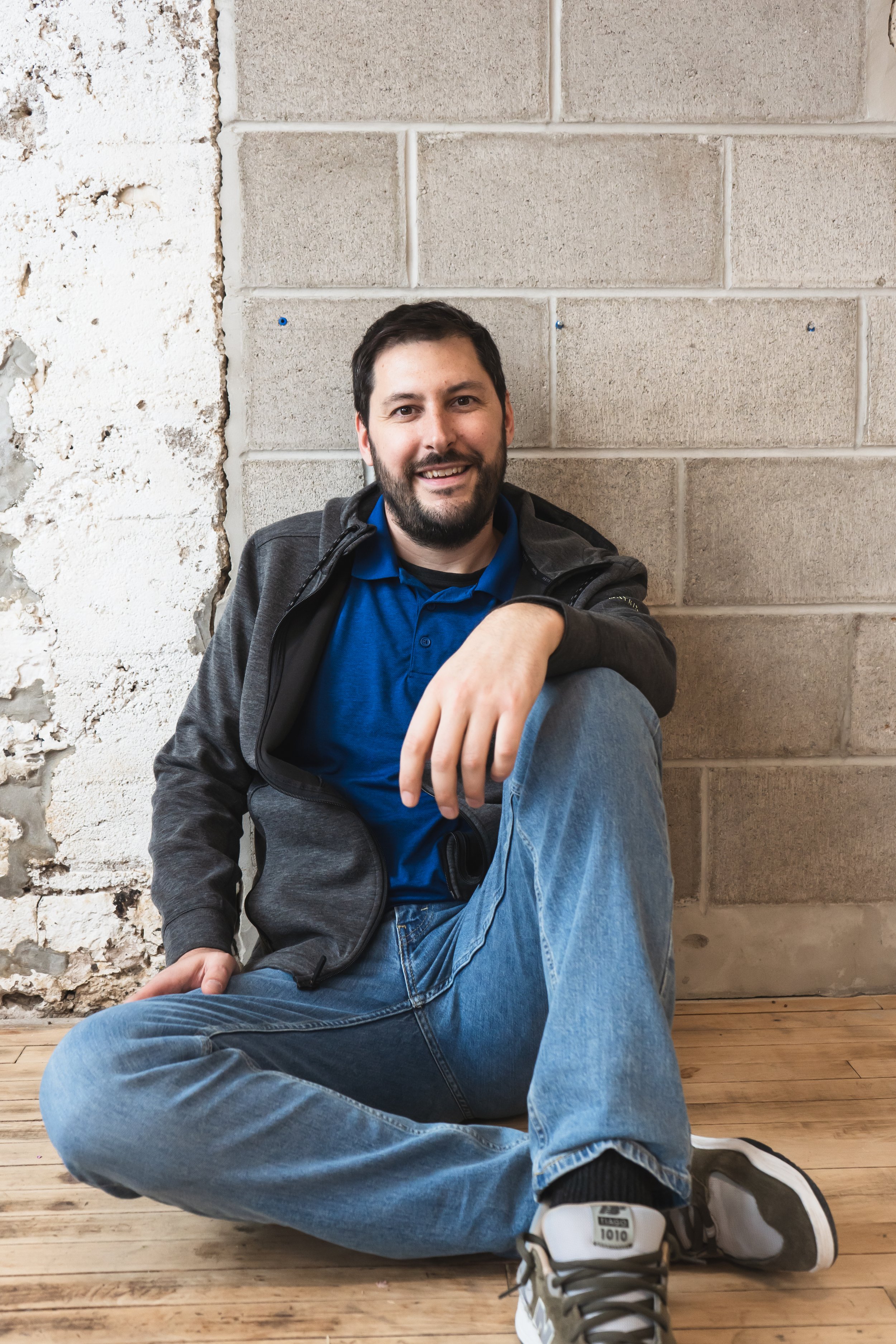 videographer from Toronto Ontario Canada sitting on the floor in front of a brick wall smiling at the camera.