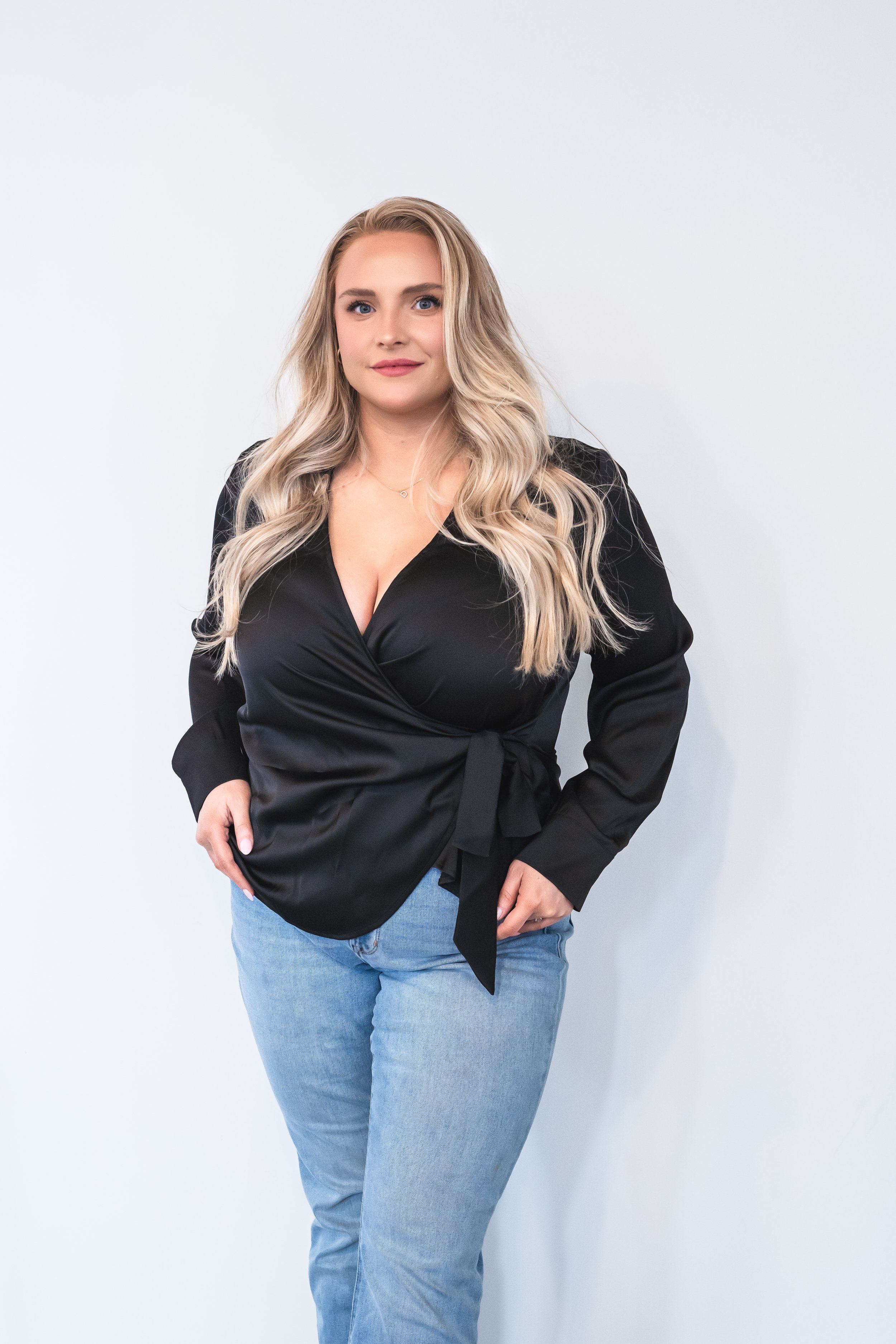 A real estate agent from Hamilton Ontario Canada posing in front of a white wall with her hands in her pockets.