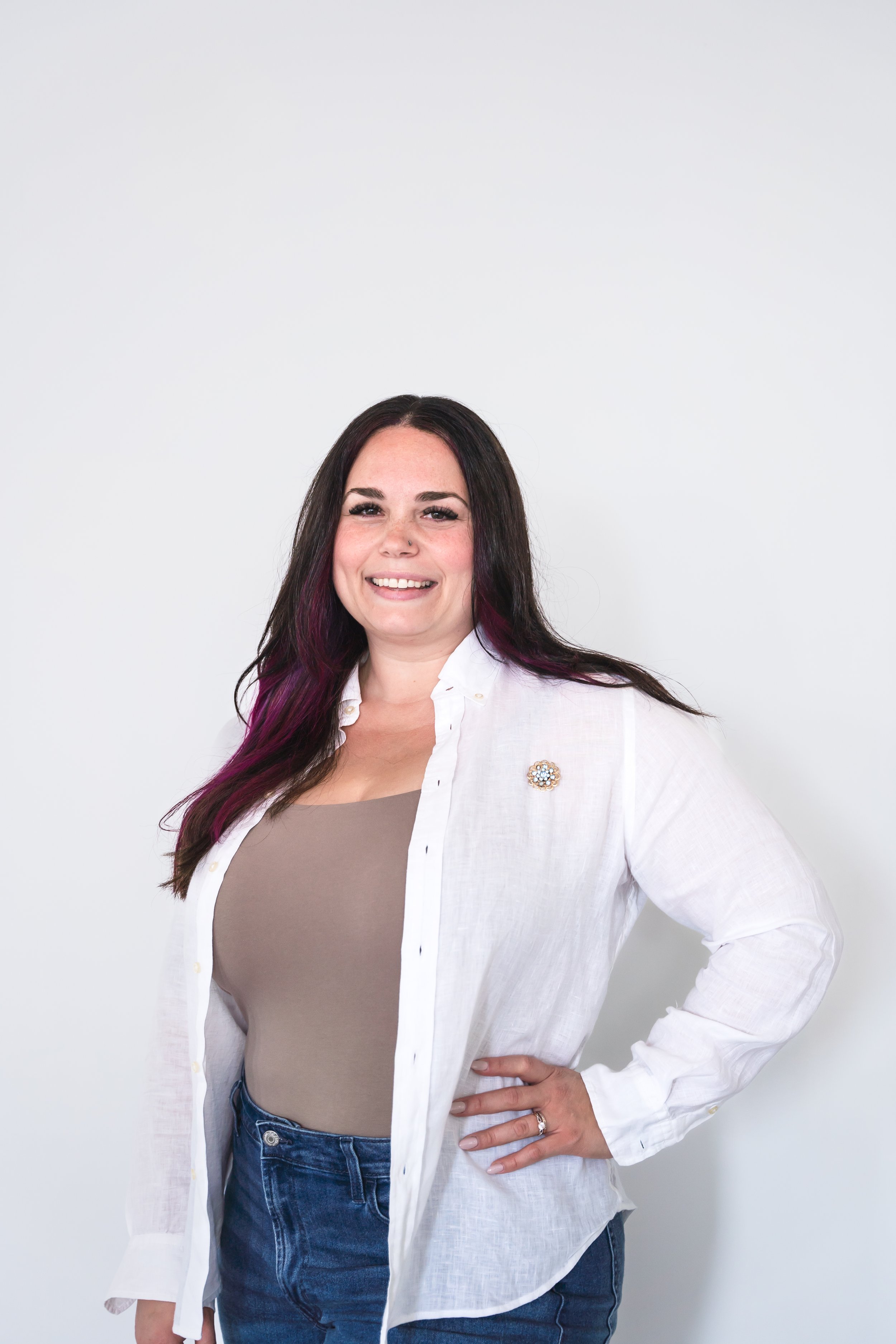 A therapist from Brantford Ontario Canada posing in front of a white wall with one hand on her hip smiling confidently at the camera.