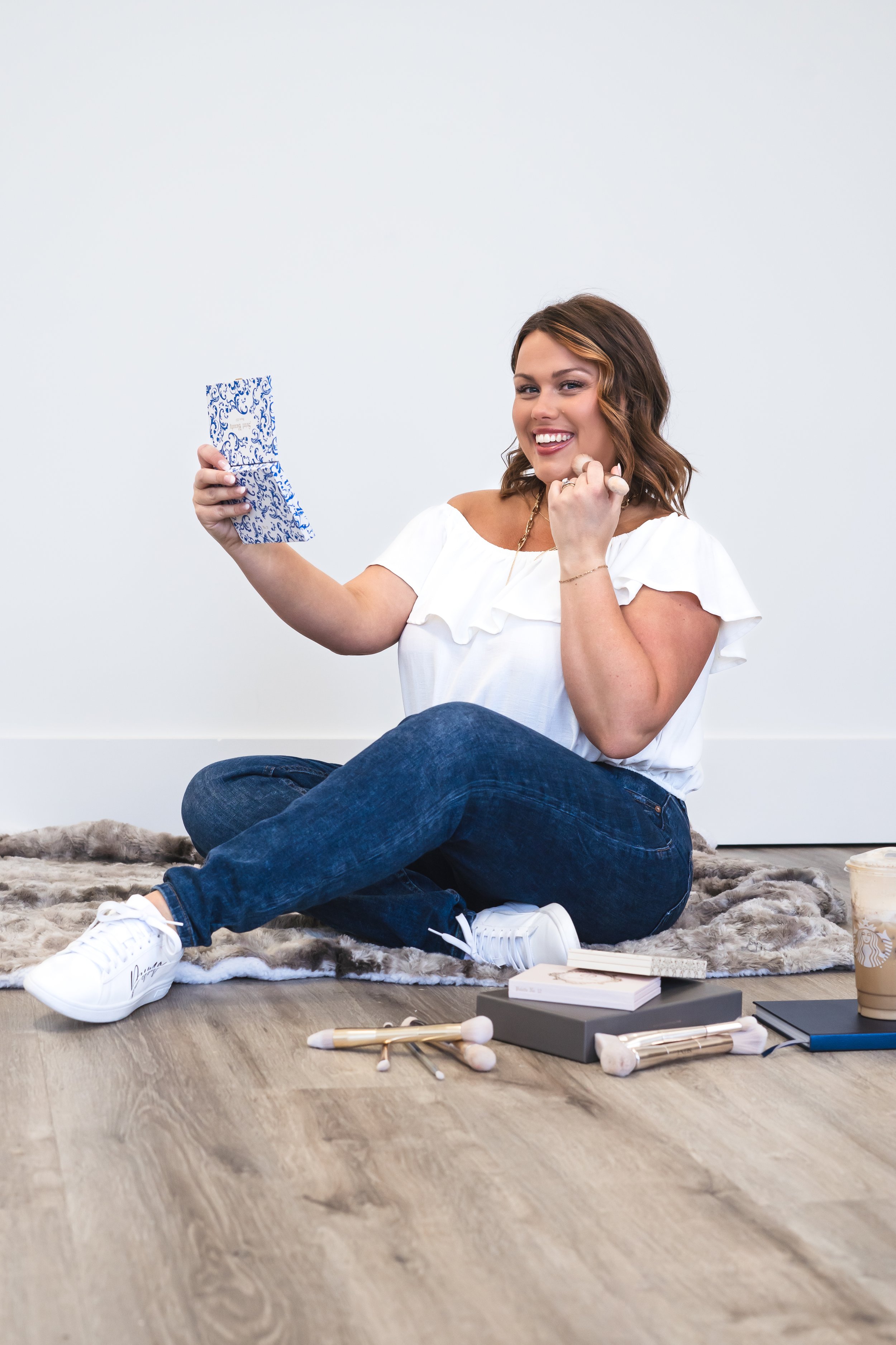 A makeup artist in London Ontario sitting on the floor with makeup spread out, holding a mirror up.