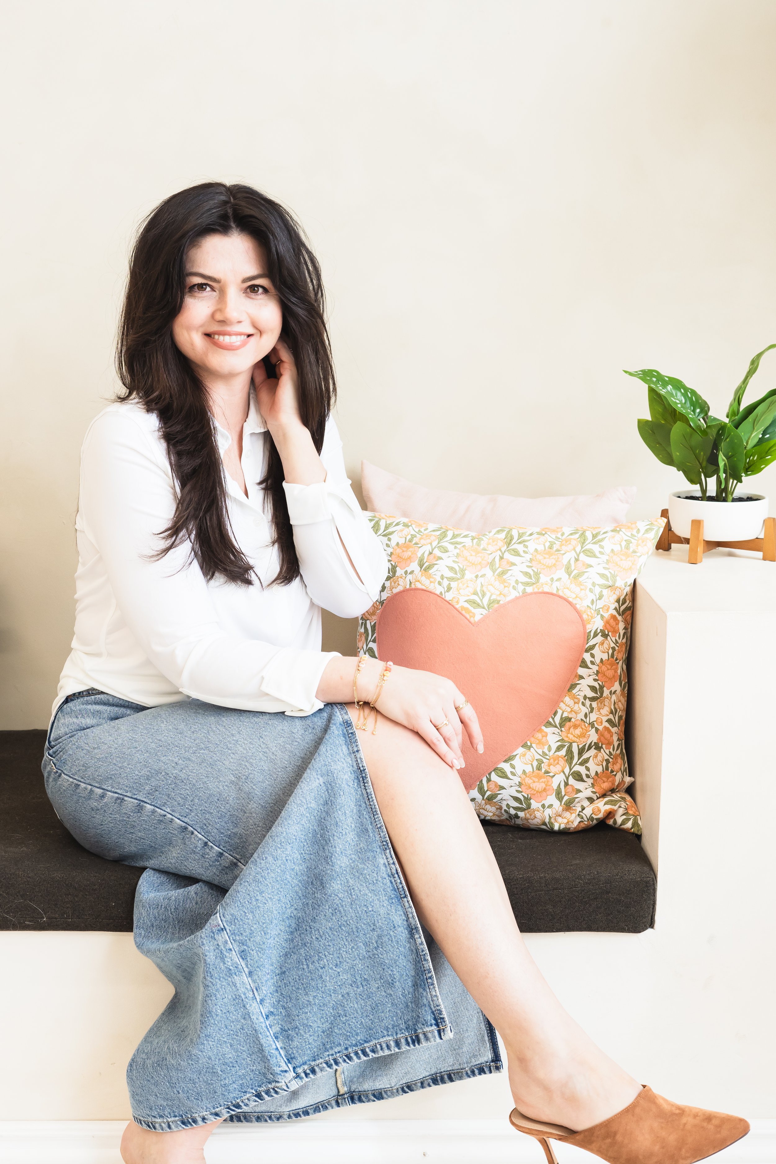 A creative business owner from Cambridge Ontario Canada posing on a bench with her legs crossed, her hand on her knee and her other hand tucking her hair back. A small potted plant beside her.