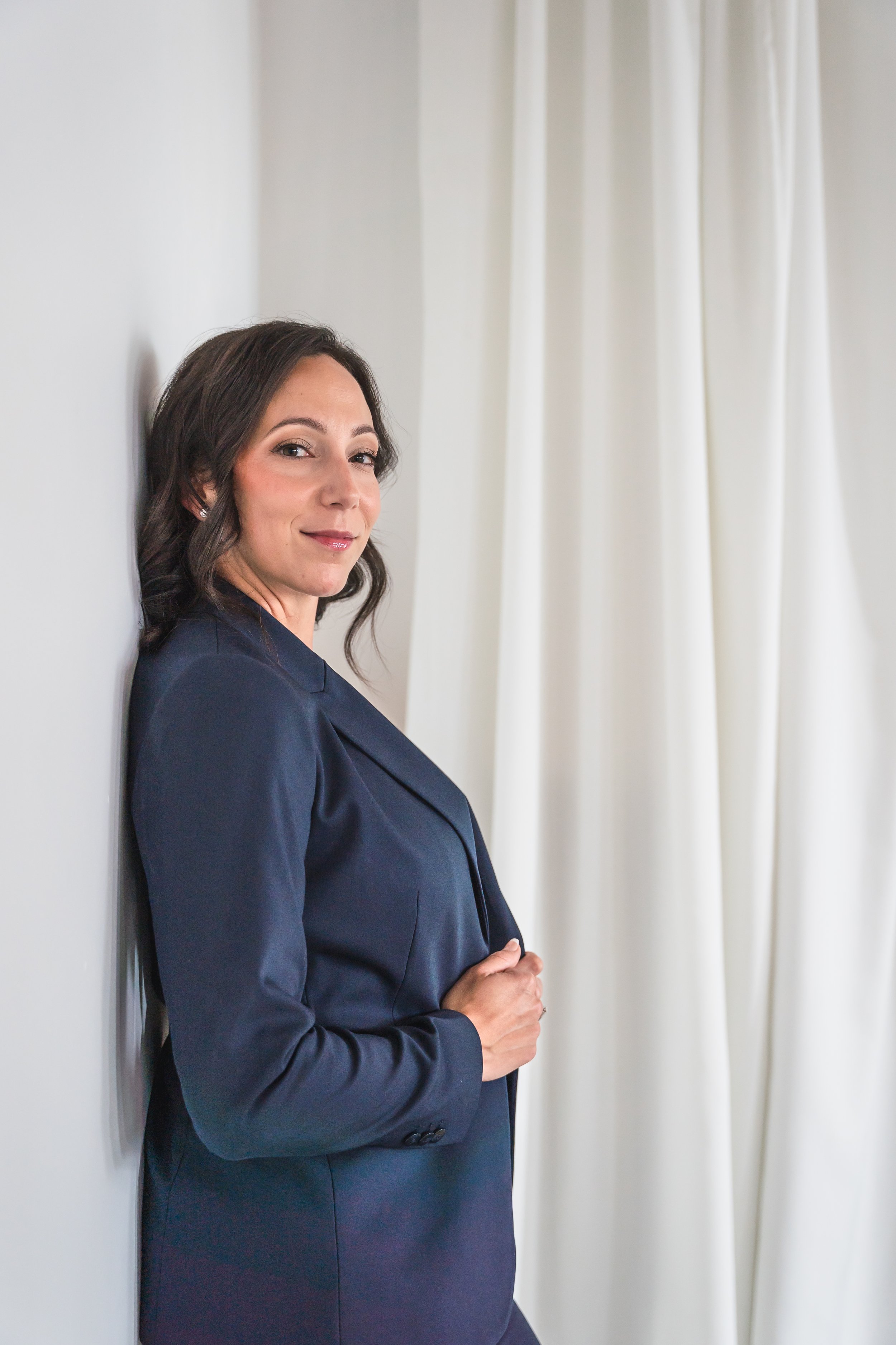 An event planner from Brantford Ontario Canada leaning up against a white wall looking sideways at the camera with a soft smile.