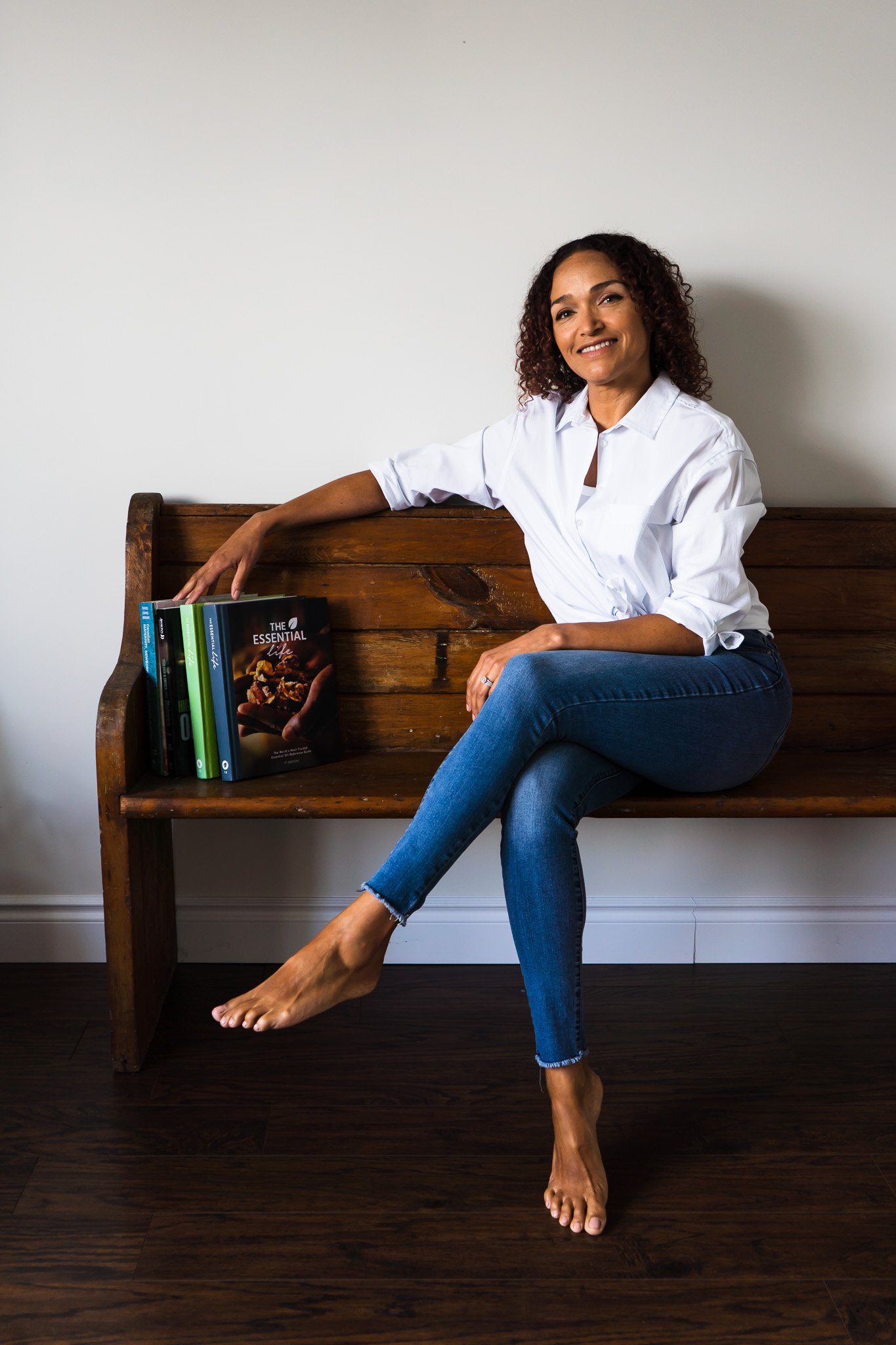 a wellness consultant from London Ontario Canada posing on a wooden bench with her legs crossed at the knee and her favourite wellness books beside her.