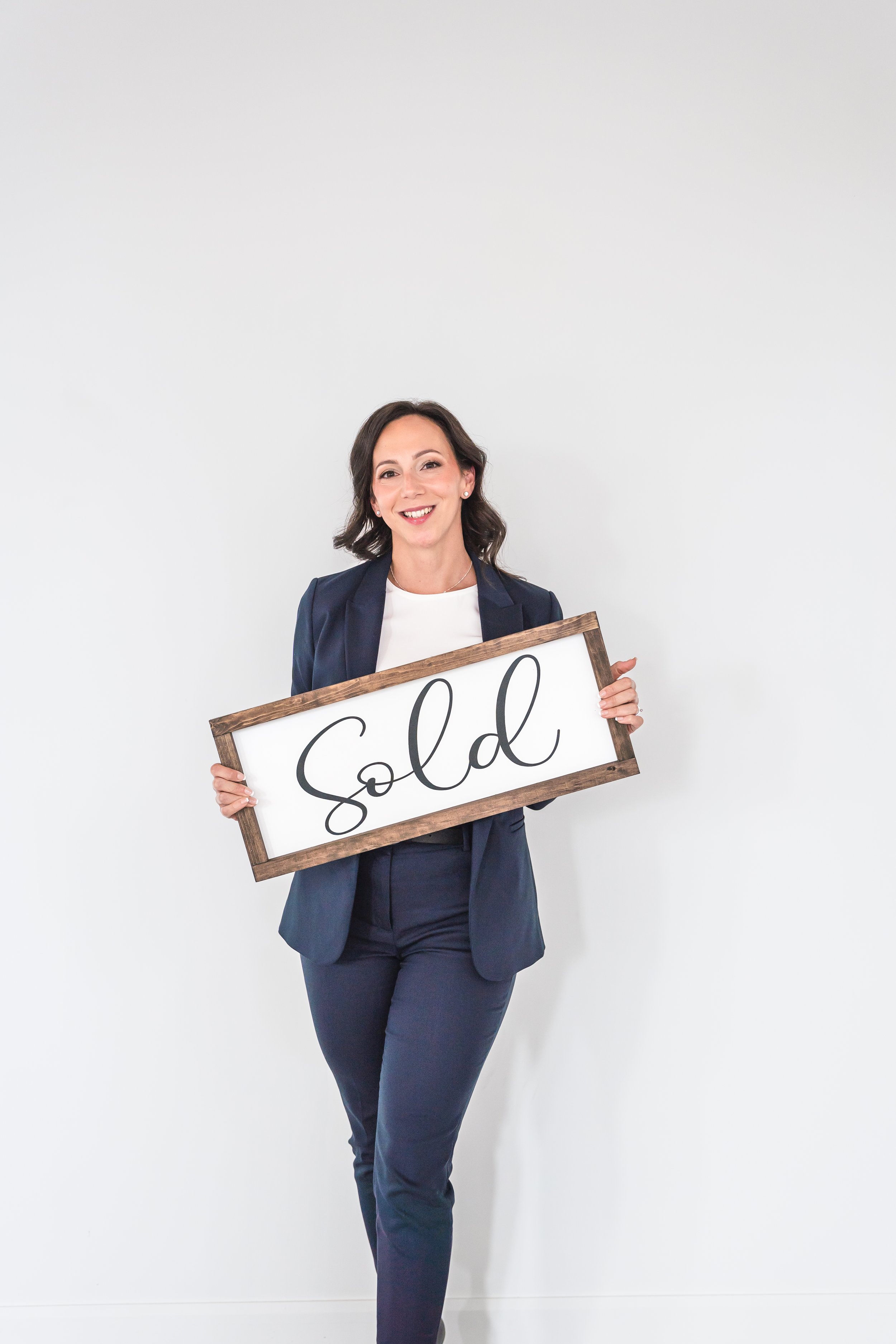 An event planner from Brantford Ontario Canada standing in front of a white wall holding a handmade wooden sign in front of her.