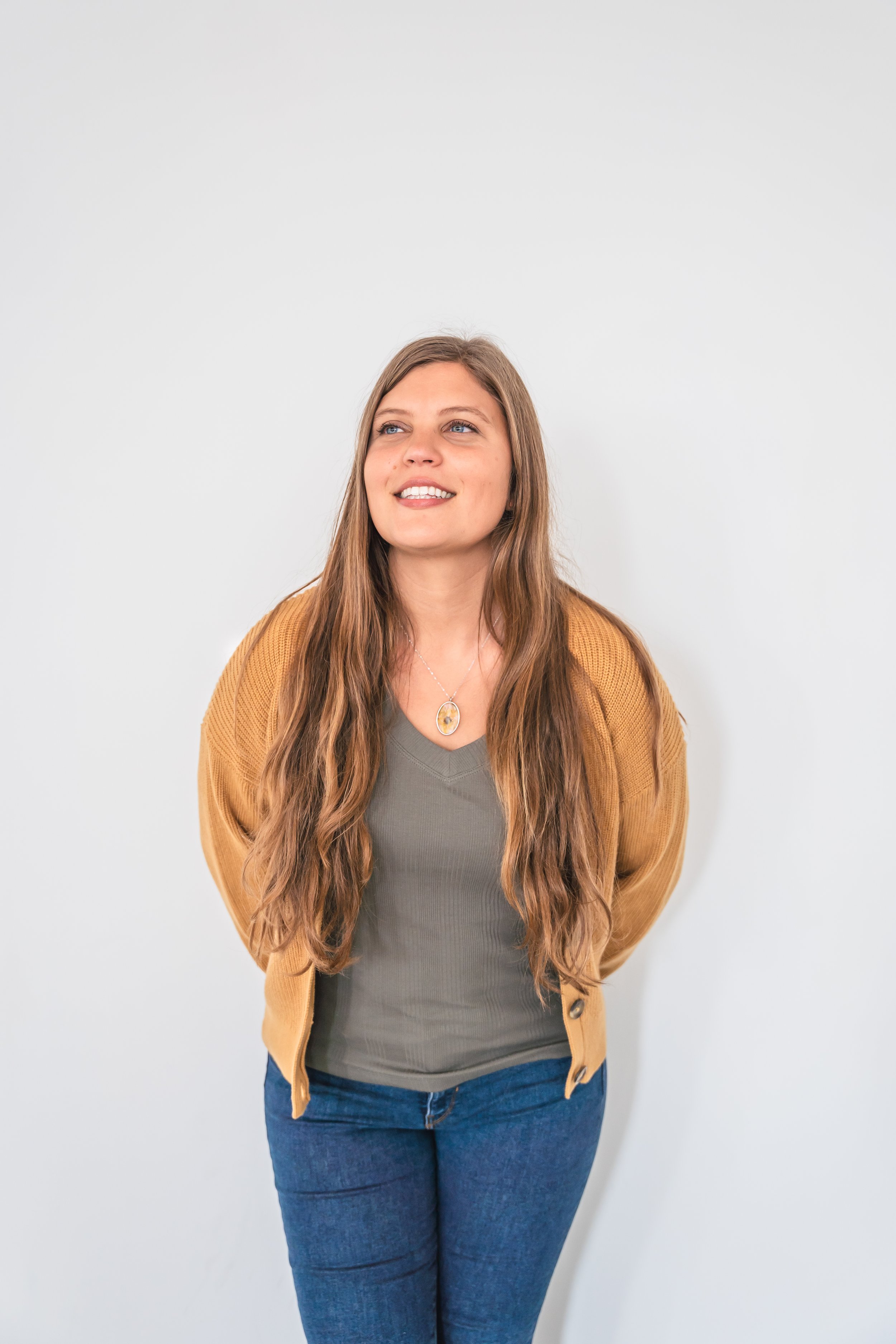 A therapist from Brantford Ontario Canada posing with her hands behind her in front of a white wall.