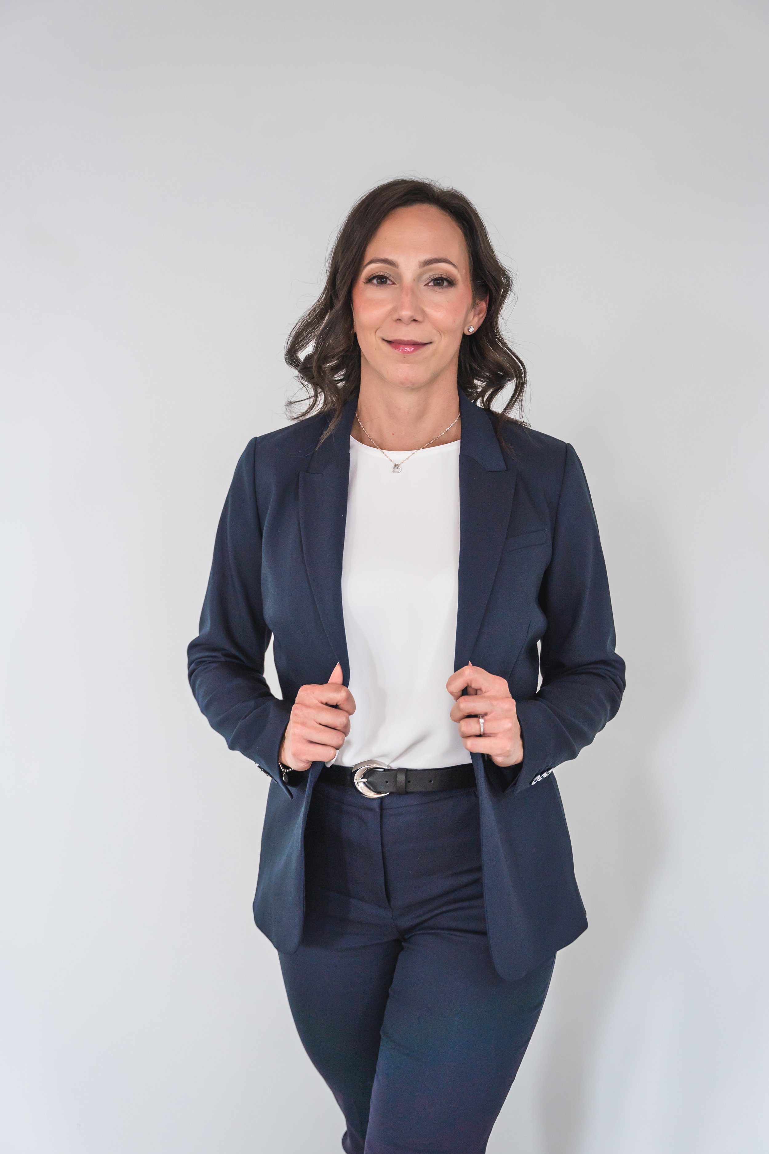 An event planner from Brantford Ontario Canada posing confidently in a power suit in front of a white wall.