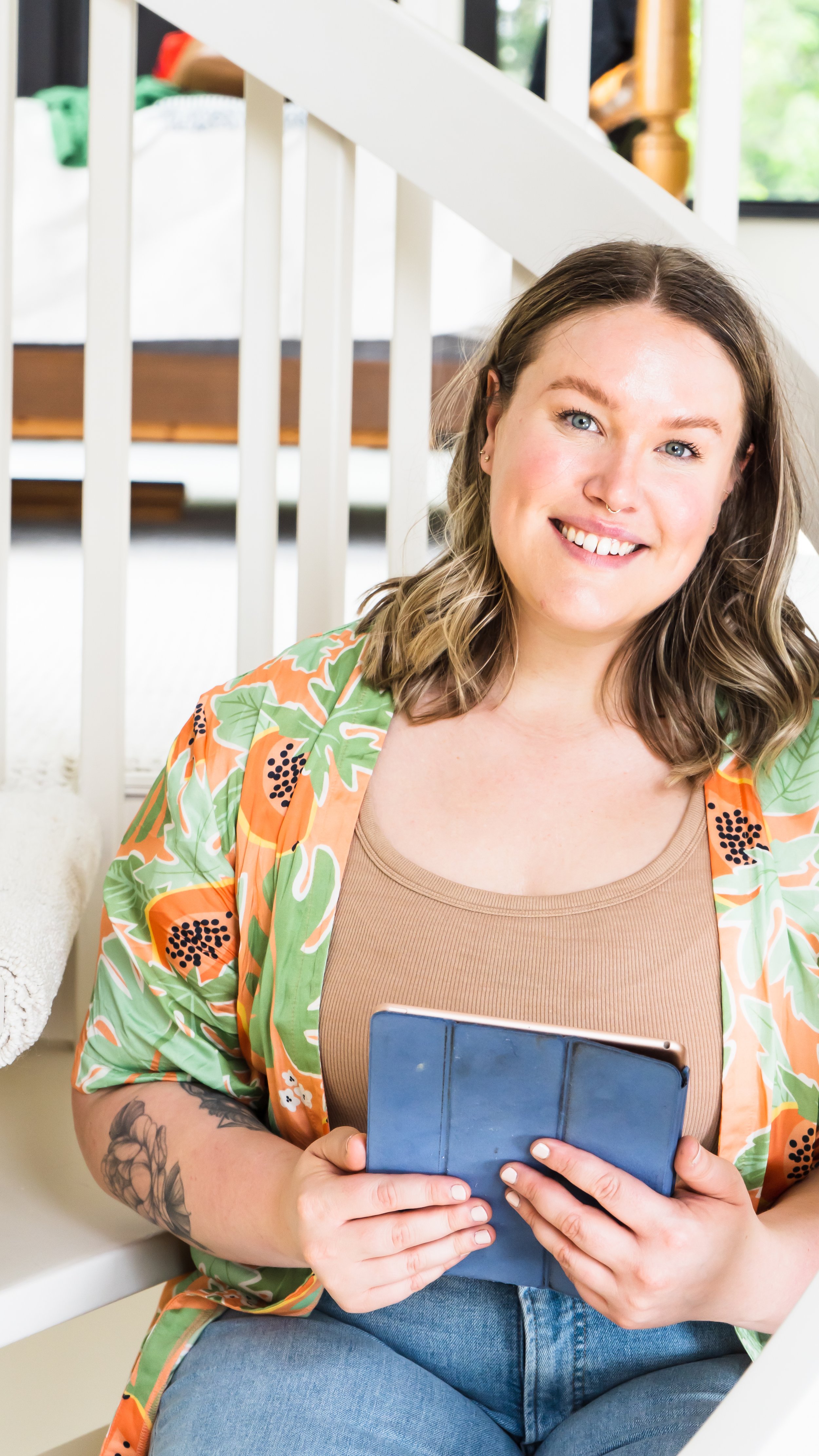 A massage therapist from Burlington Ontario Canada posing on a white spiral staircase, holding an iPad in her hand and smiling softly at the camera.