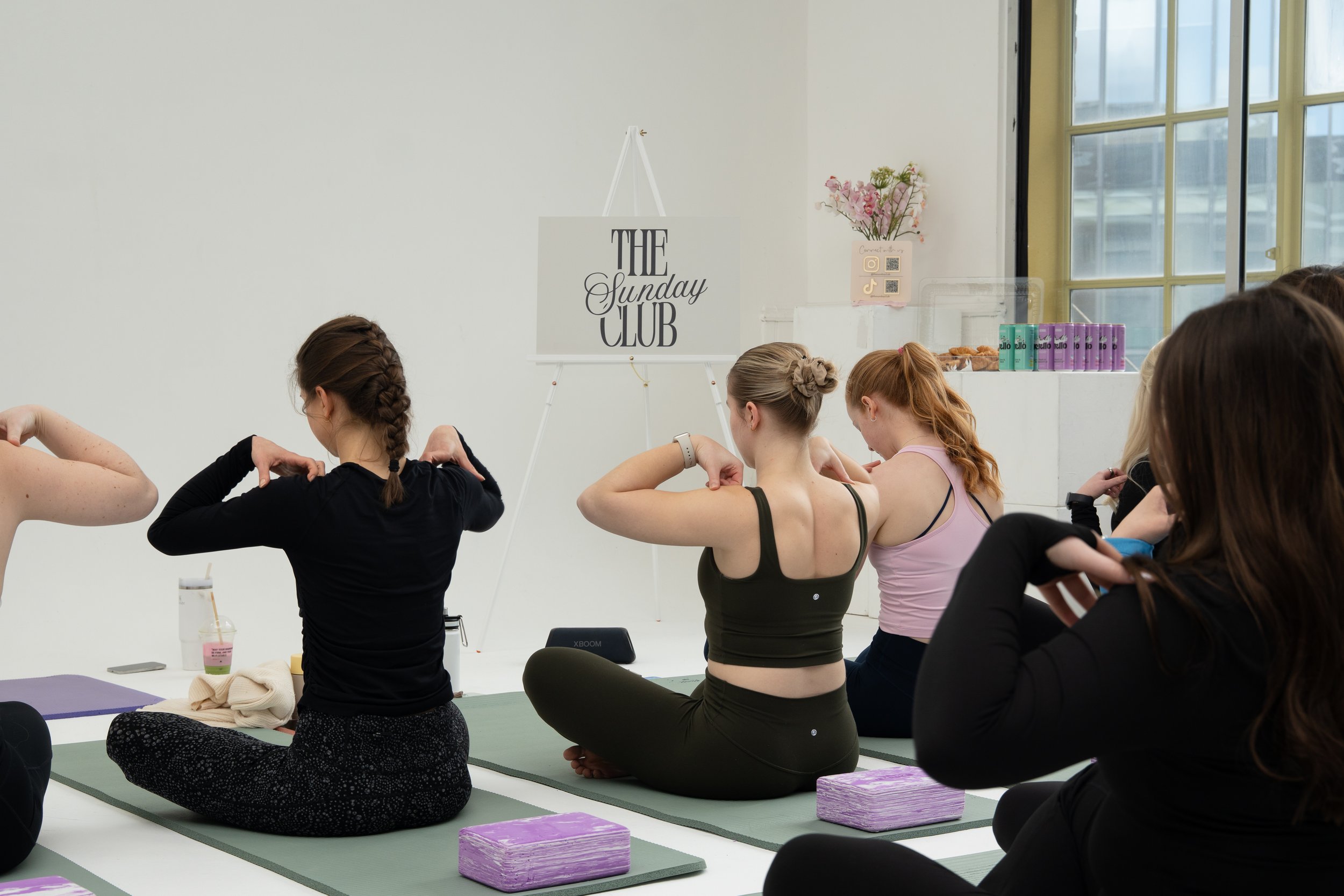 Group of women practicing yoga indoors, sitting cross-legged on mats with eyes closed and hands in a prayer position, during a yoga class.