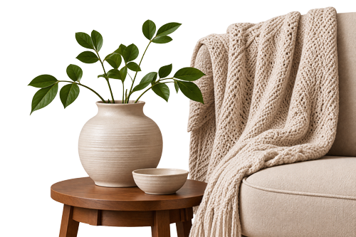 A photo of a couch with a throw rug over it next to an endtable that has a potted plant and a small bowl.