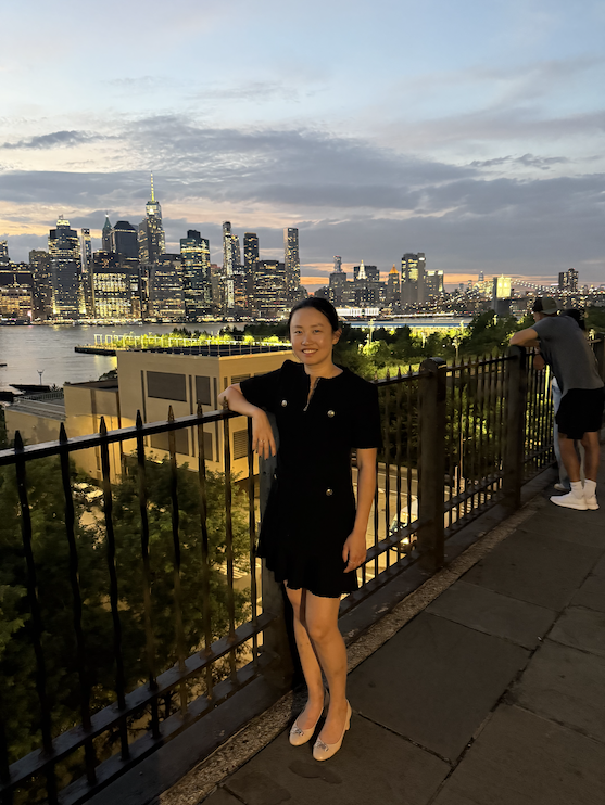 Judy Zhou on the Brooklyn Heights promenade, with the skyline of Manhattan in the background.
