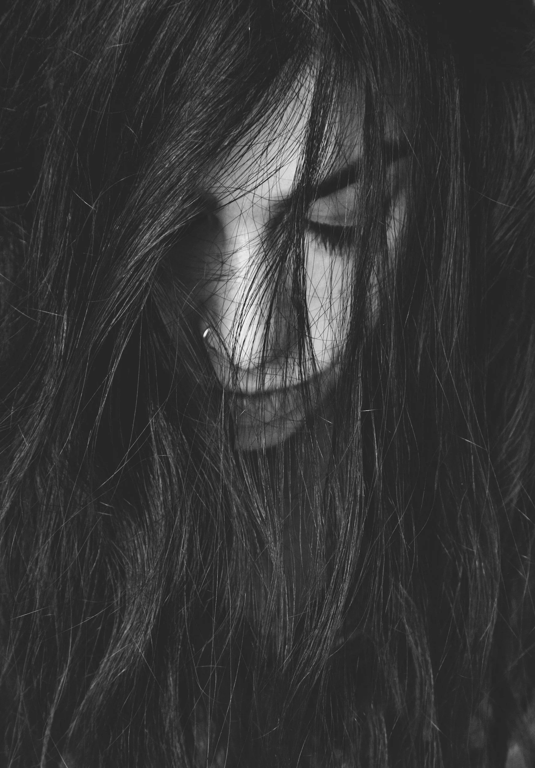 Black-and-white close-up of Jamie Hann, Temple Wellness founder and San Diego hair extension & holistic wellness specialist, with long hair covering her face, eyes closed, and a subtle nose piercing