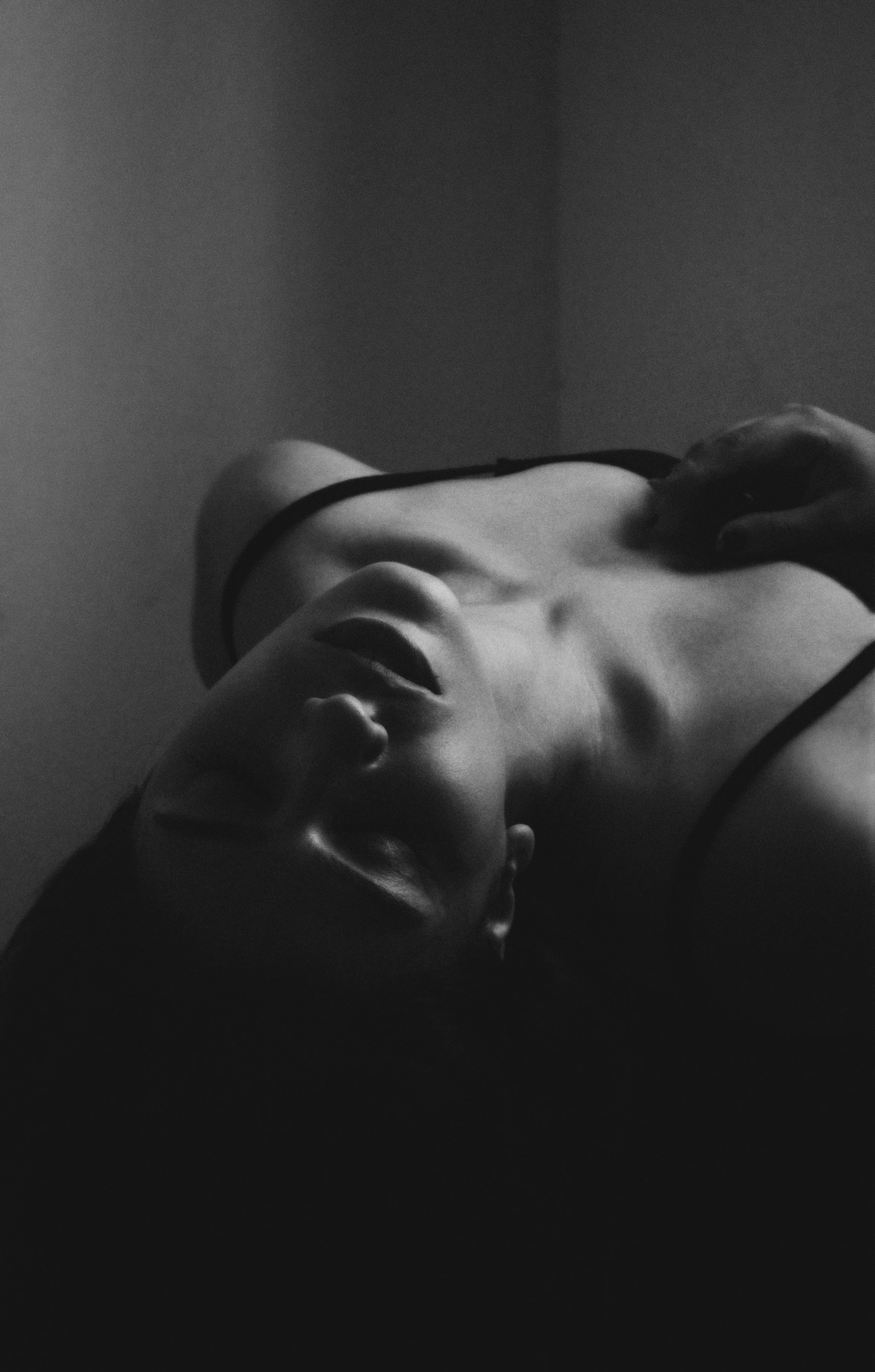 Black-and-white image of a somatic breathwork participant at Temple Wellness; a woman in a spaghetti-strap top lying on her back with eyes closed, hand on chest and head tilted back, embodying deep relaxation and holistic healing