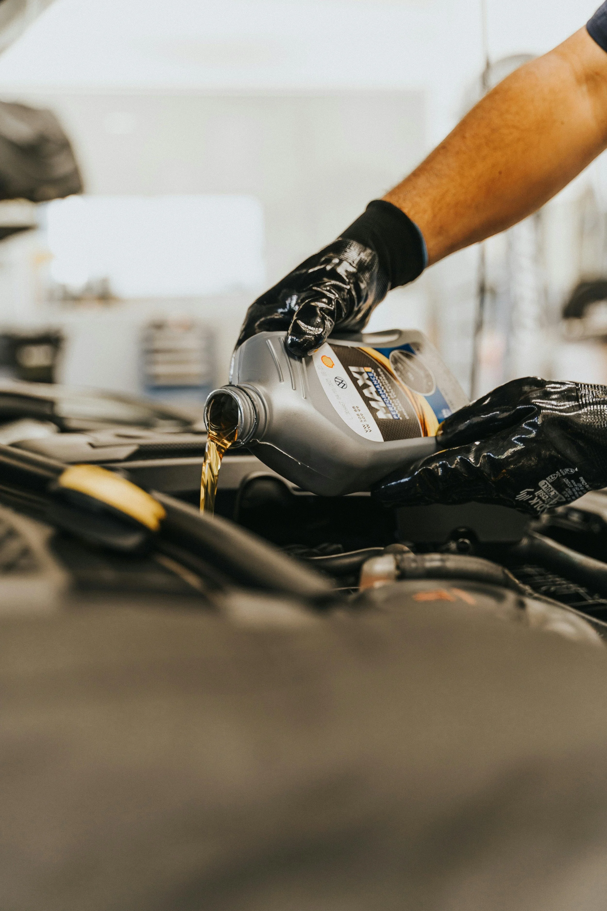 A person wearing black gloves pouring motor oil into a car engine.