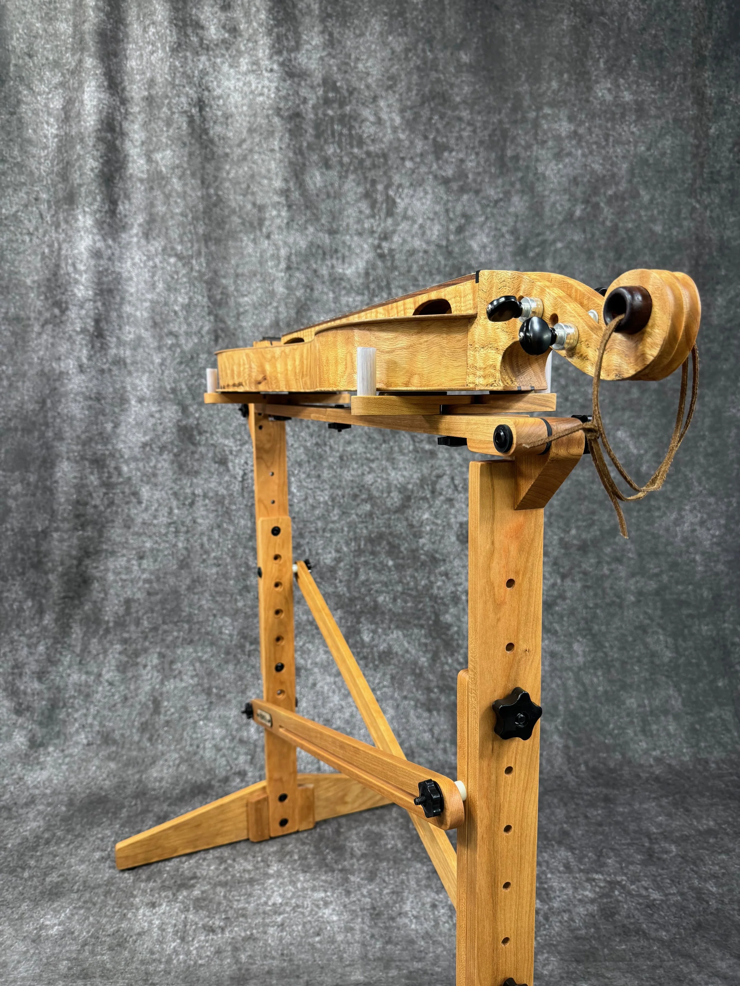 A closeup view of the tuning pegs of a mountain dulcimer on a dulcimer stand.