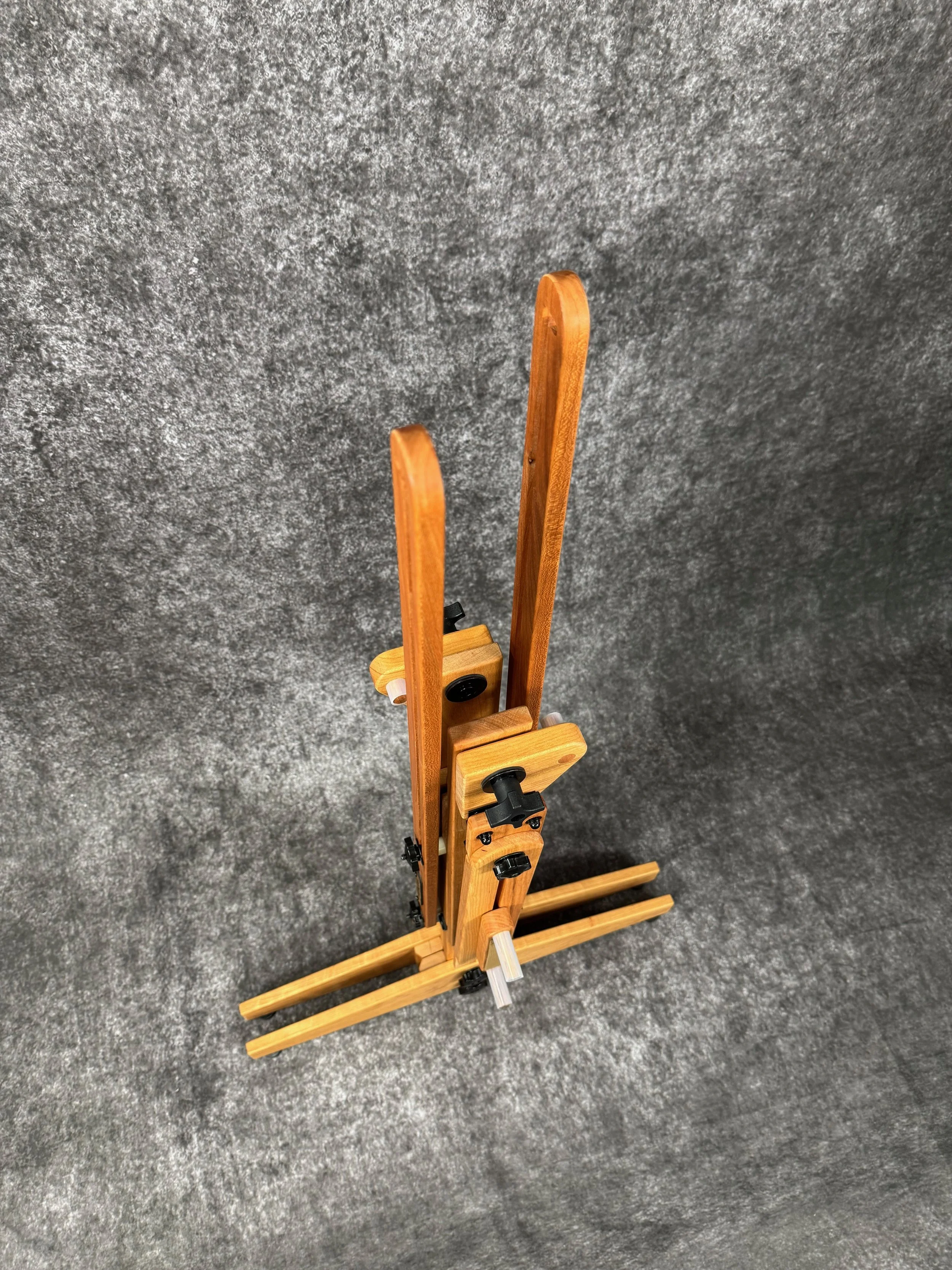 A folded mountain dulcimer stand, standing on a textured gray surface, viewed from above.