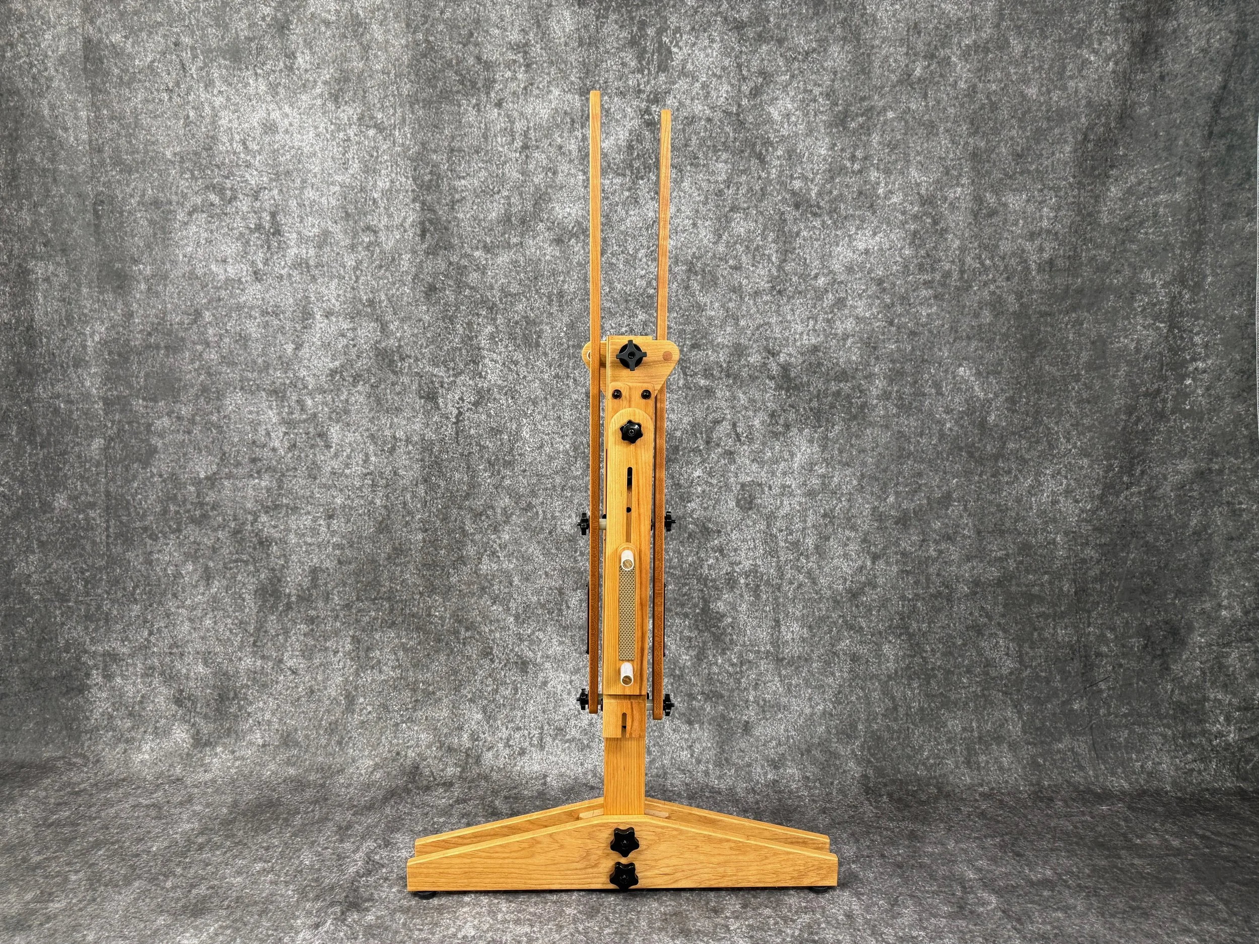A folded mountain dulcimer stand, standing on a textured gray surface, viewed from the side.
