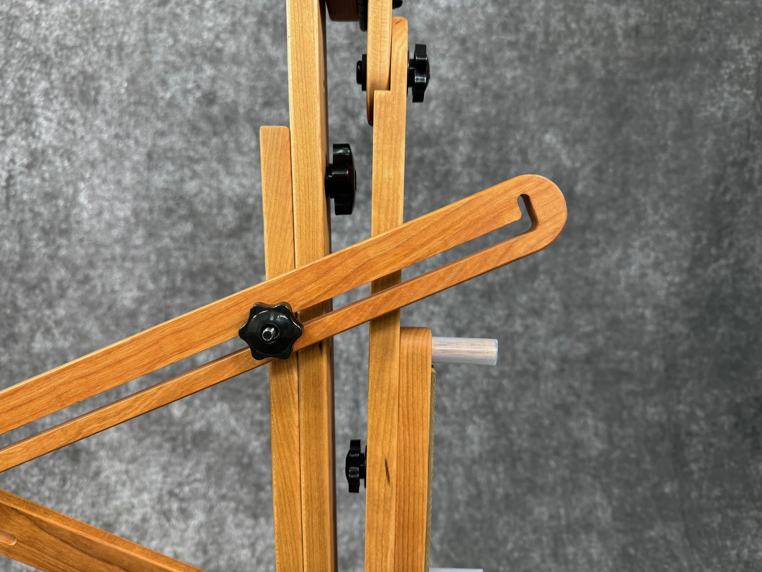 A close-up view of a wooden slide-loc x-brace, with black adjustable knobs.