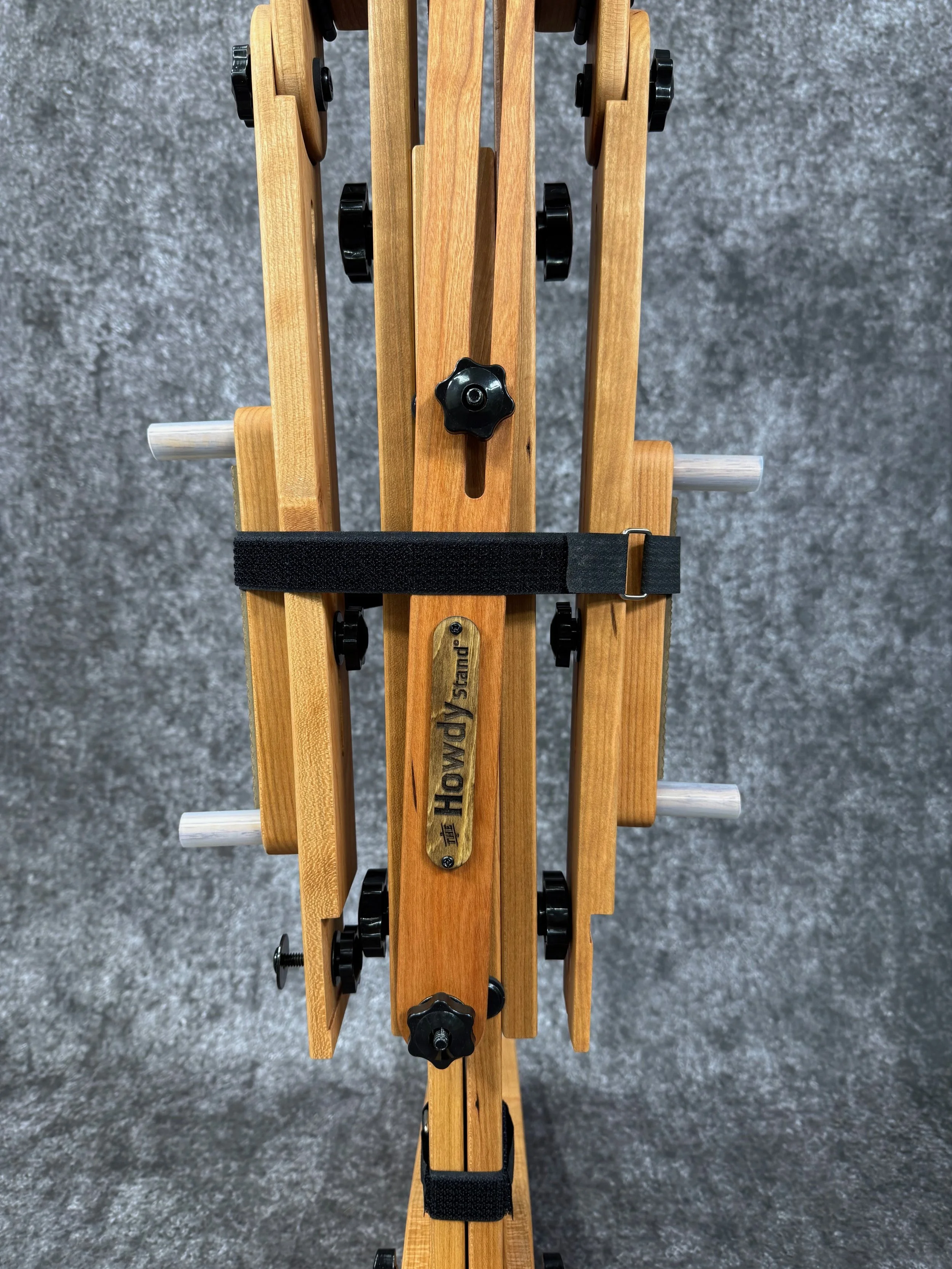 A close-up view of a folded mountain dulcimer stand with adjustable black knobs, and held together with black hook and loop straps.