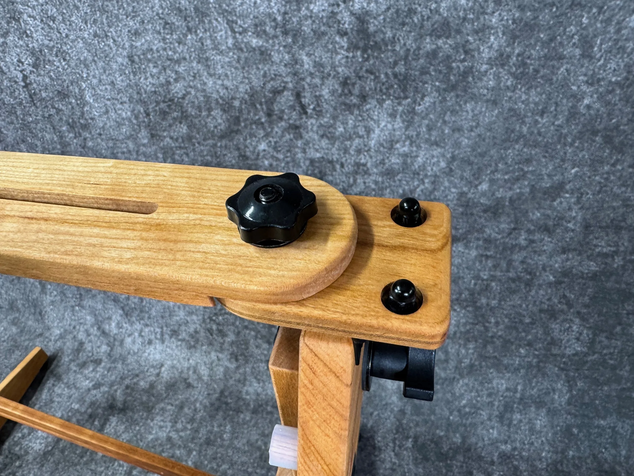 Close-up image of a mountain dulcimer stand swivel plate, with a black knob and other black components.