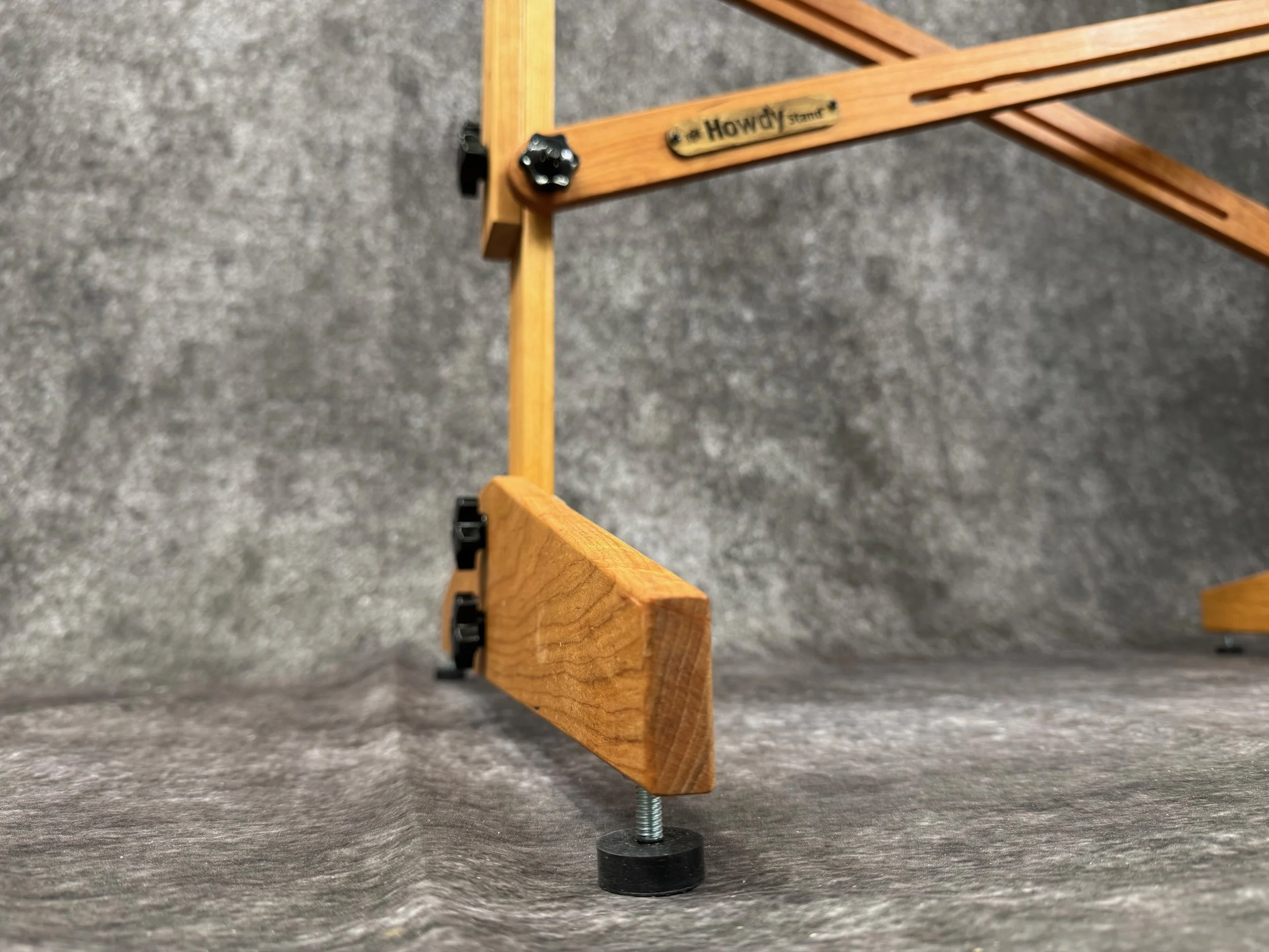 Close-up of the adjustable furniture feet of a mountain dulcimer stand, labeled 'Howdy' with black knobs.