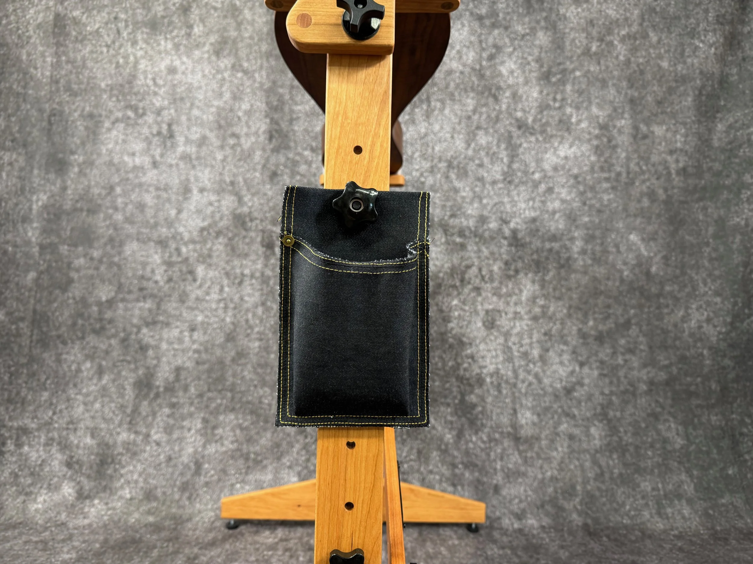A view of a black denim accessory pouch, attached to the leg of a wooden mountain dulcimer stand.