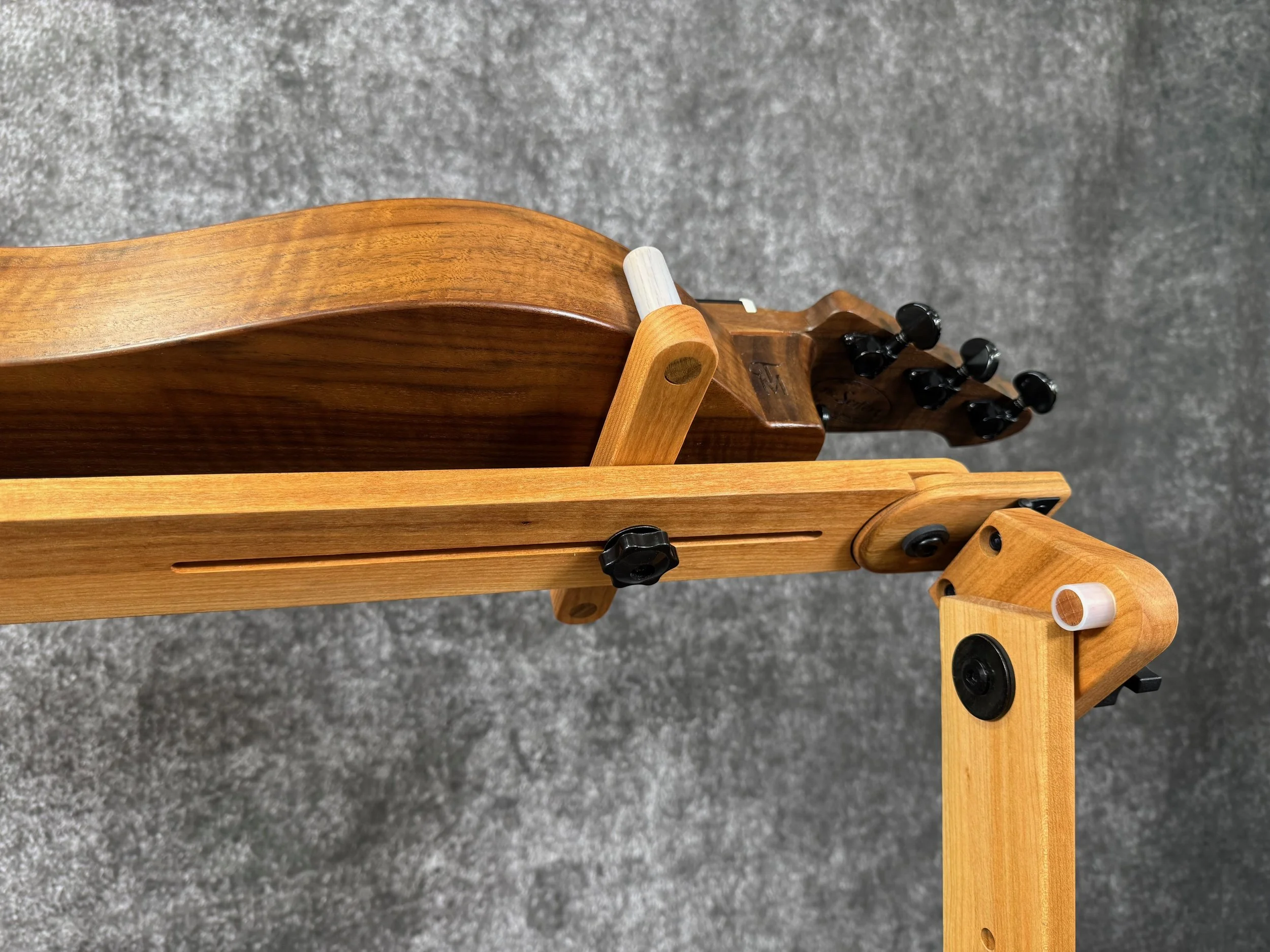 A close-up view of the peghead end of amountain dulcimer on a wooden stand, tilted at an angle, with black knobs.