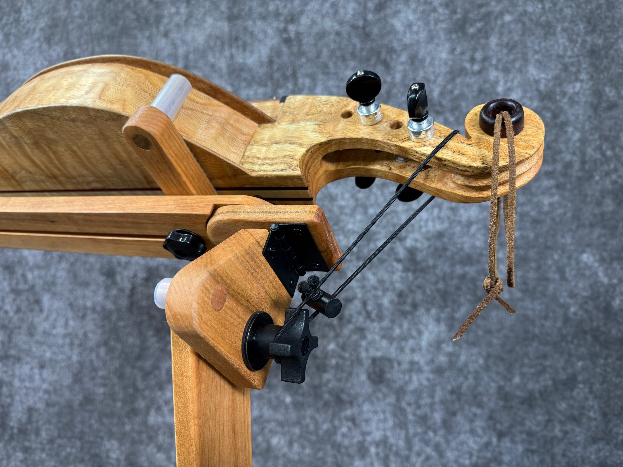 Close-up of a scroll-head mountain dulcimer, on a tilted wooden stand, secured by a wooden brace and small bungee cord.