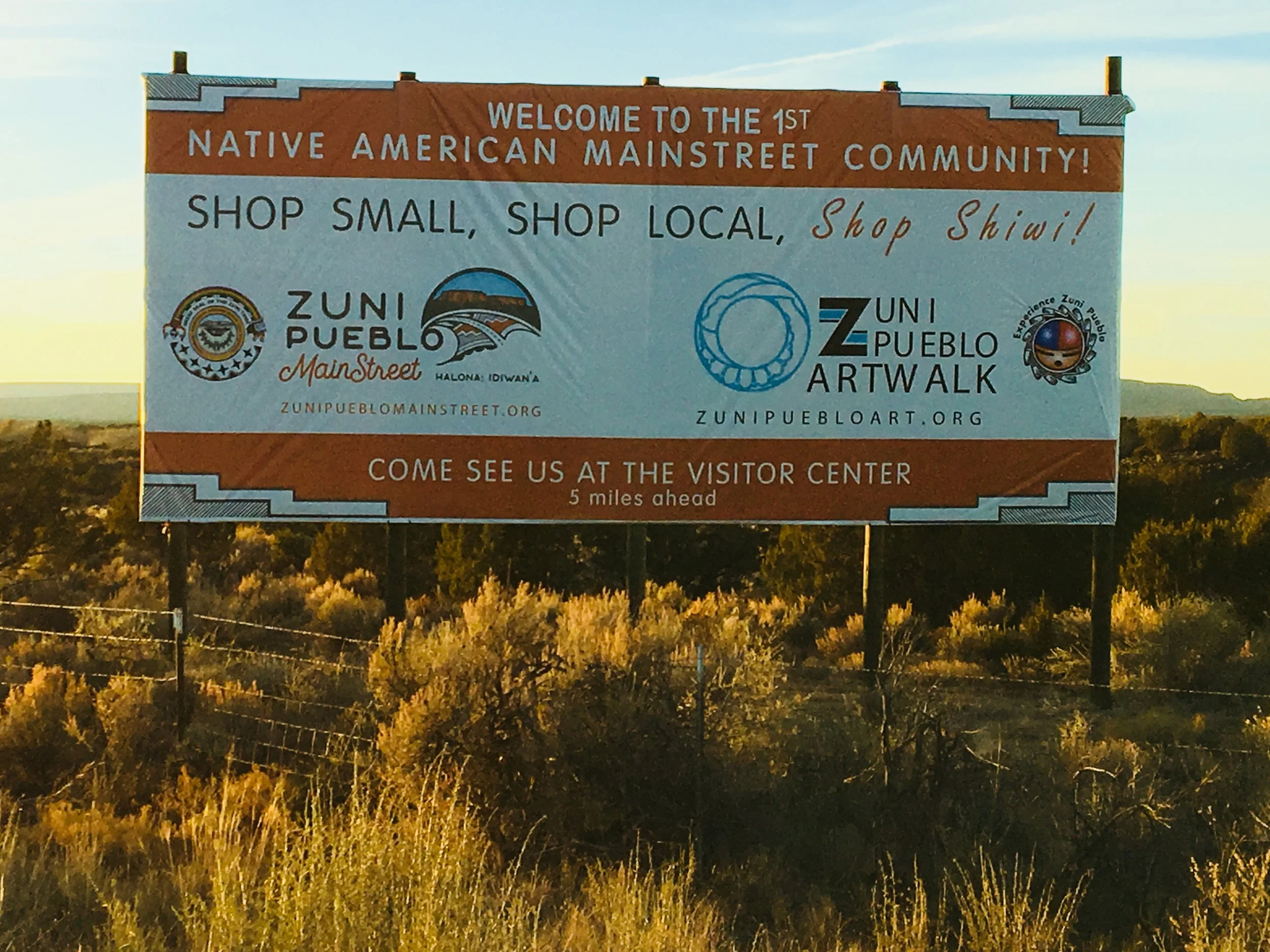 Young woman in construction uniform and orange safety helmet standing in front of construction trucks at a work site.