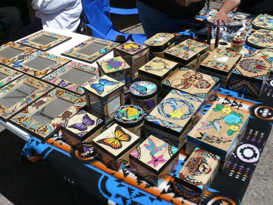Colorful wooden jewelry boxes with butterfly and floral designs displayed on a table at a market.