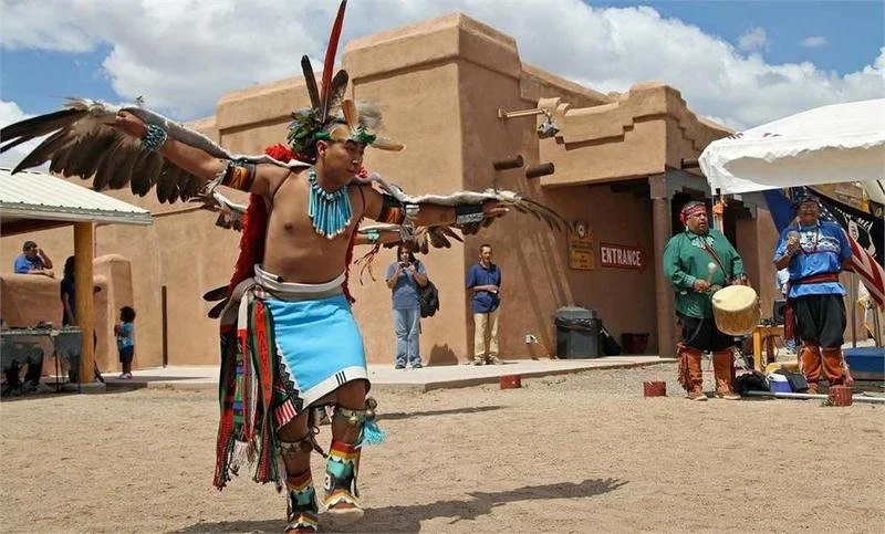 Native American dancer wearing traditional regalia with feathers and beadwork, performing a dance outdoors at a cultural event.