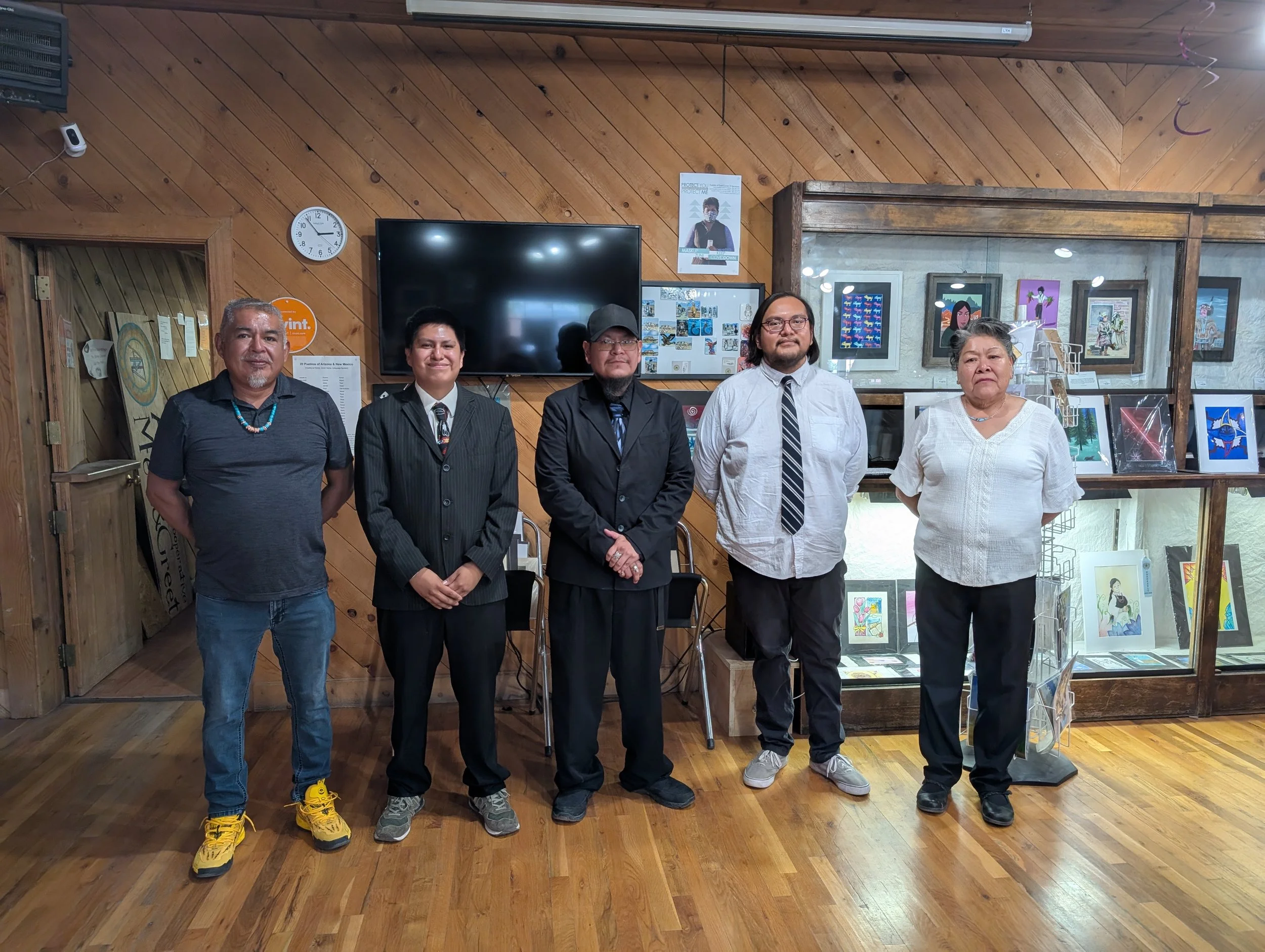 A woman in traditional maid attire with a white bonnet and black dress, standing outdoors with trees in the background, a small white house with a thatched roof, and mountains in the distance.