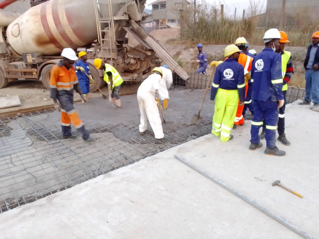 Workers are pouring concrete and placing rebar on a construction site.