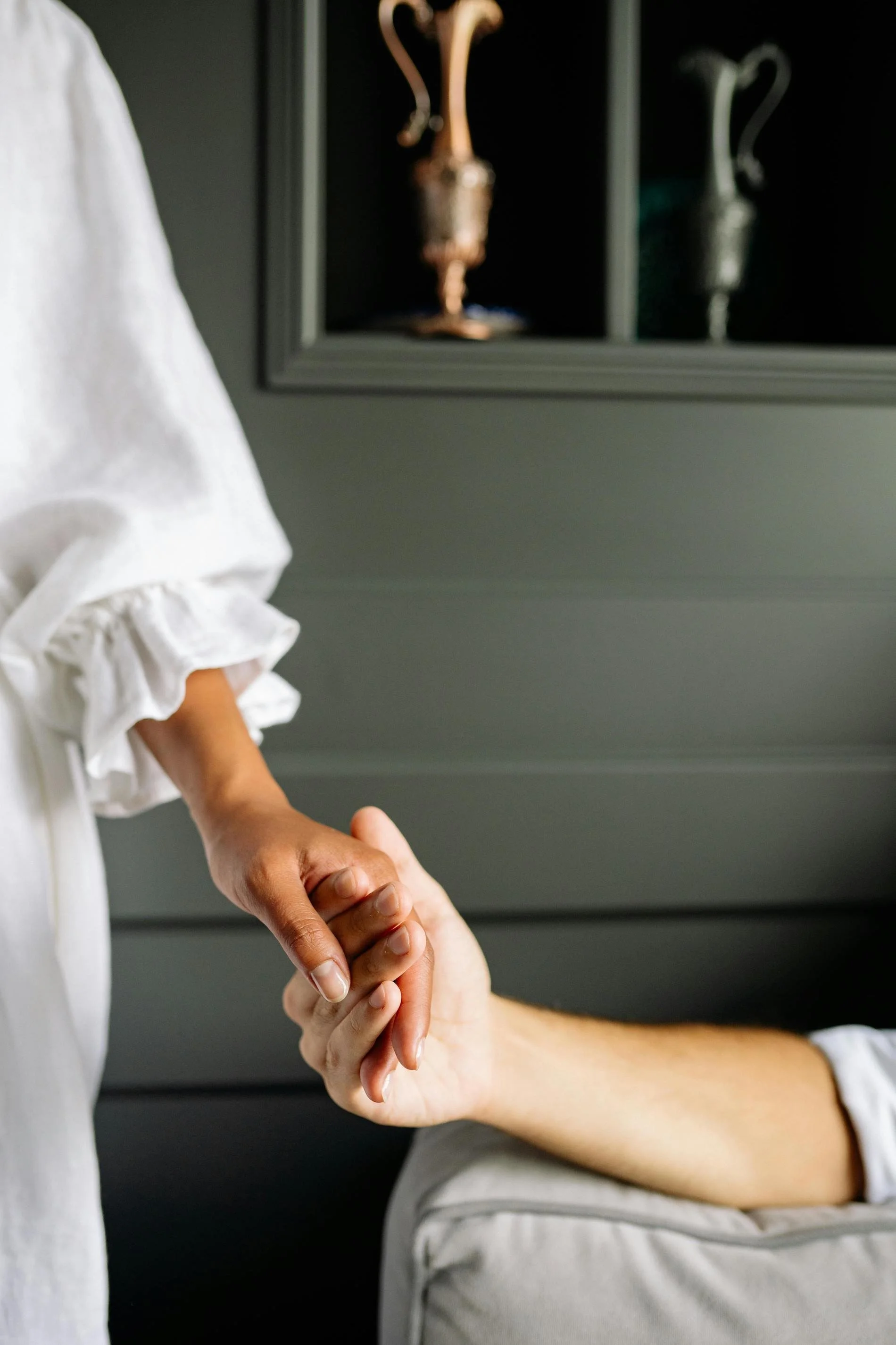 A person in a white shirt holding hands with another person, with a framed display of antique utensils in the background.
