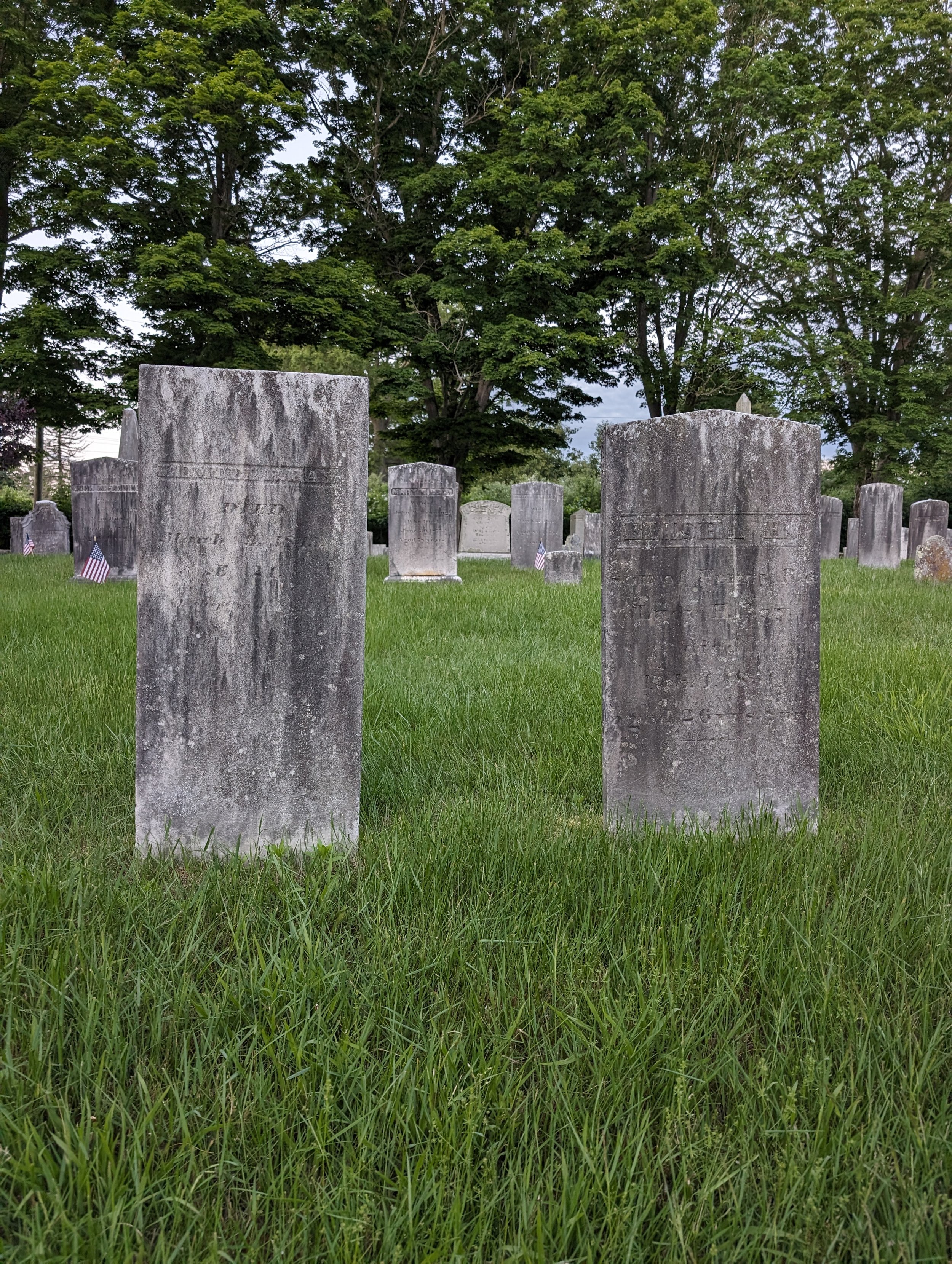 Two worn headstones made from grey stone. Headstones mark the graves of Lemuel and Elisha Ray.
