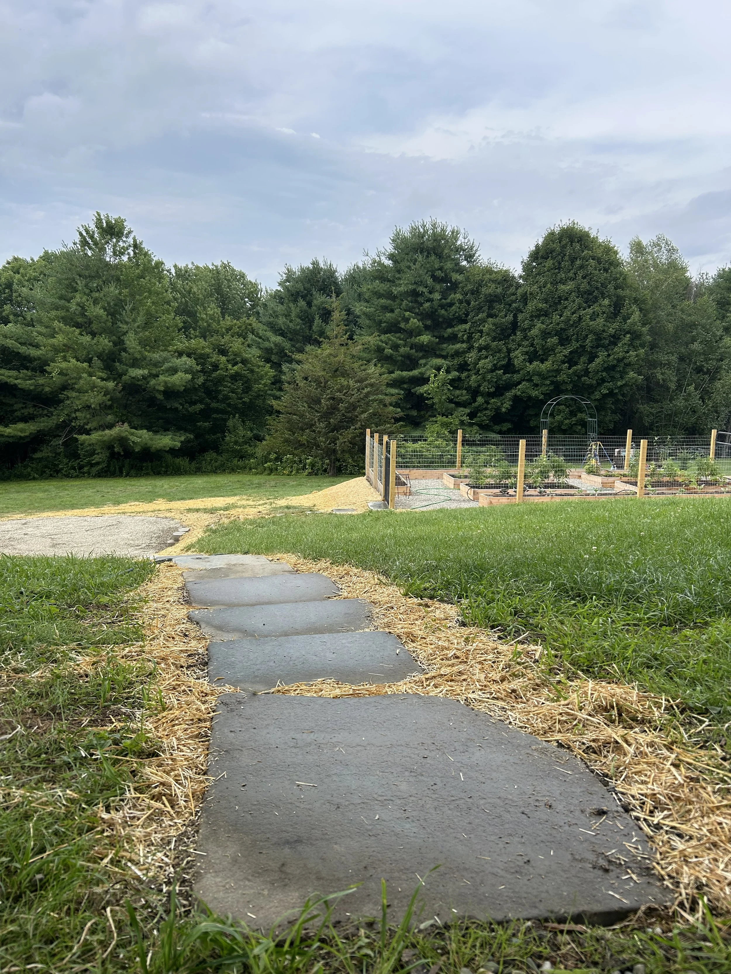 Stepping stones, pea stone firepit area and a raised vegetable garden with a fence around