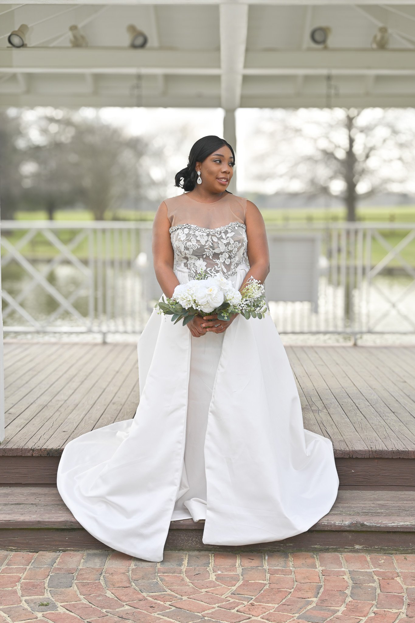 Elegant bride in a white wedding gown holding a bouquet, posing under a gazebo in Rocky Mount, North Carolina, captured by Noel Butler Photography.