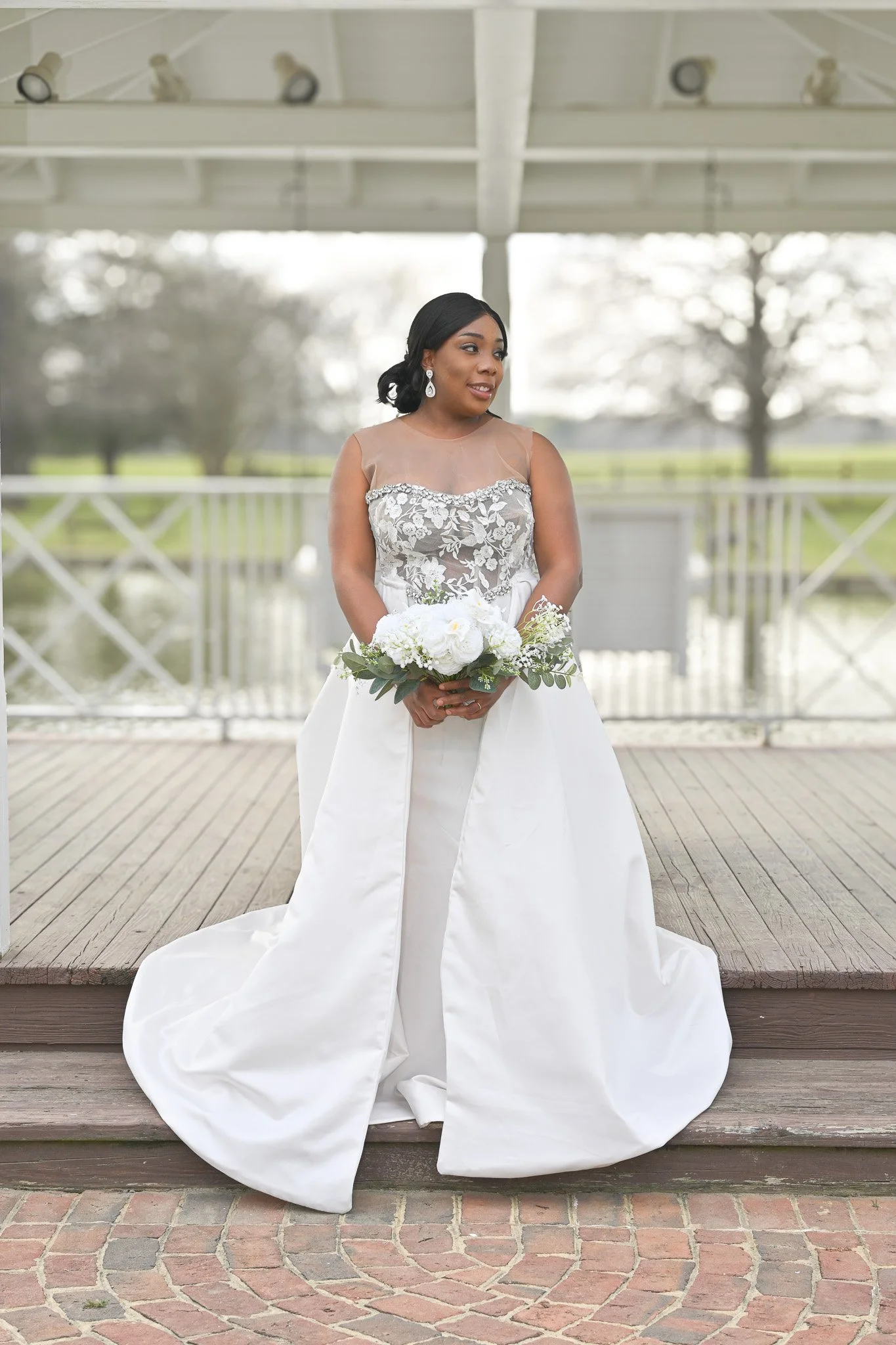 Elegant bridal portrait of a bride in a lace gown holding a bouquet under a gazebo, captured in a romantic outdoor setting by Noel Butler Photography in Rocky Mount, North Carolina.