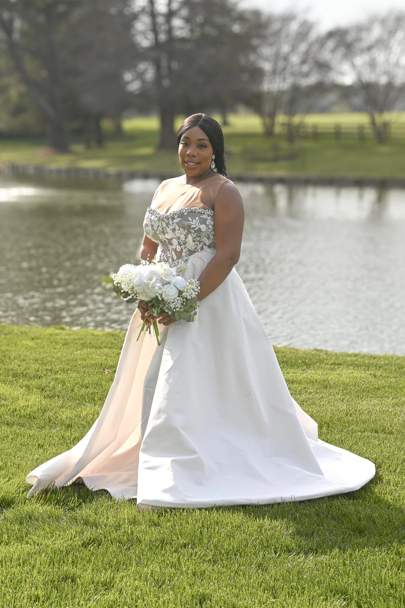 Stunning bride standing by a lakeside in a flowing wedding dress, showcasing natural beauty and timeless elegance, photographed in Rocky Mount, NC by Noel Butler Photography.