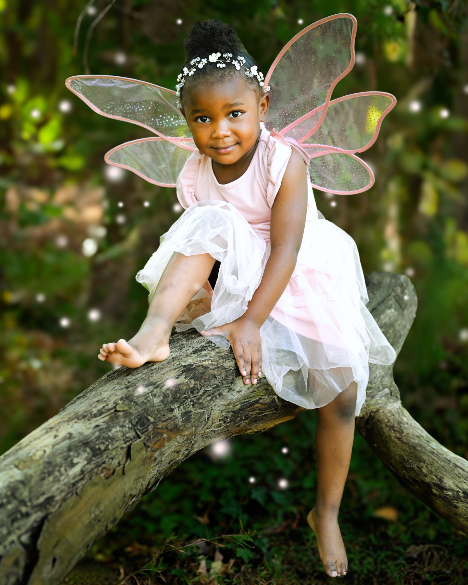 Young girl dressed as a fairy with delicate wings sitting on a tree branch outdoors, captured in a whimsical child portrait session by Noel Butler Photography in Rocky Mount, North Carolina.