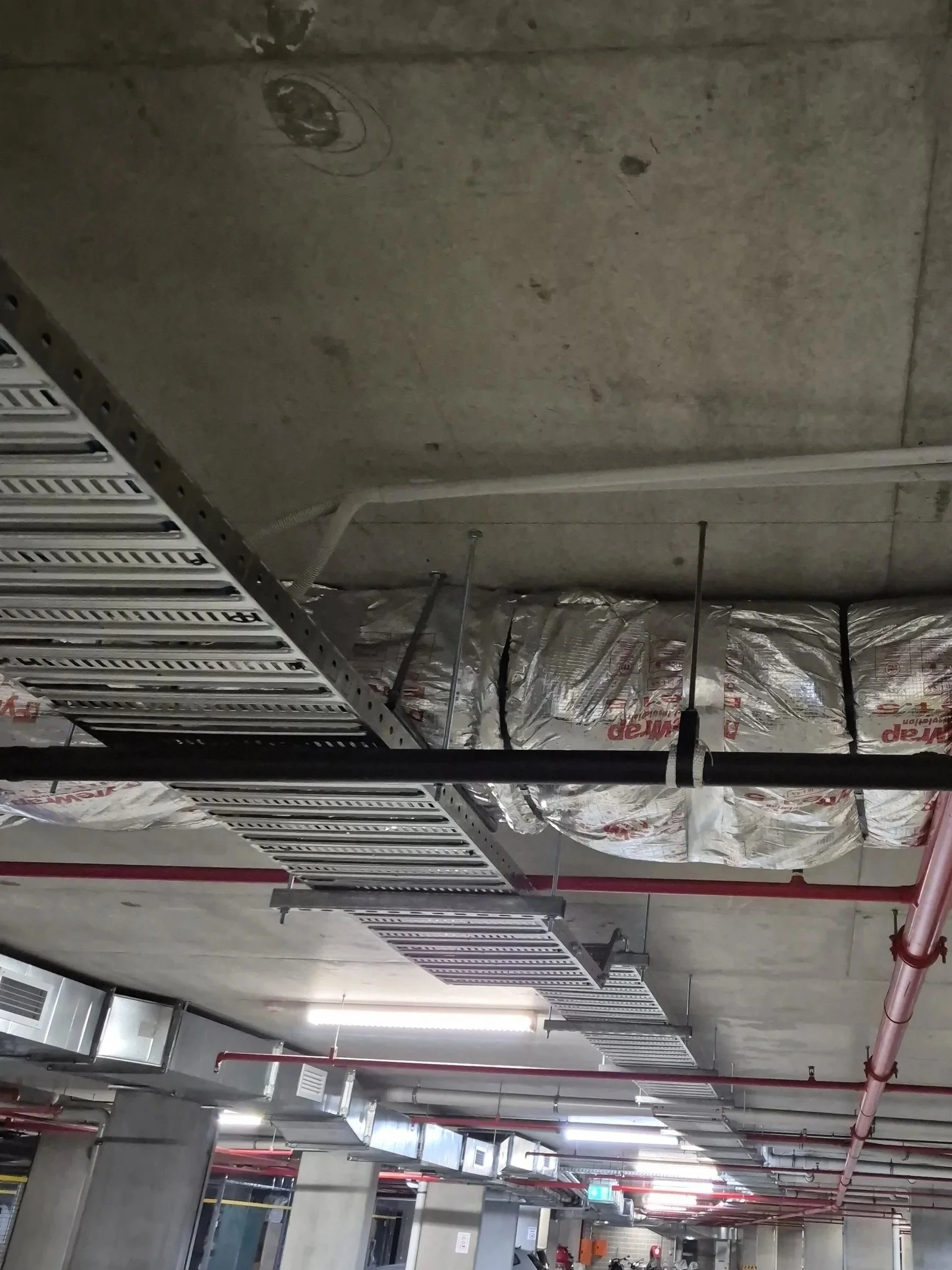 Ceiling of an underground parking garage with exposed ductwork, electrical wiring, and sprinkler pipes.