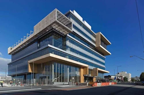 Modern multi-story office building with glass windows and angular architectural design under a clear blue sky.