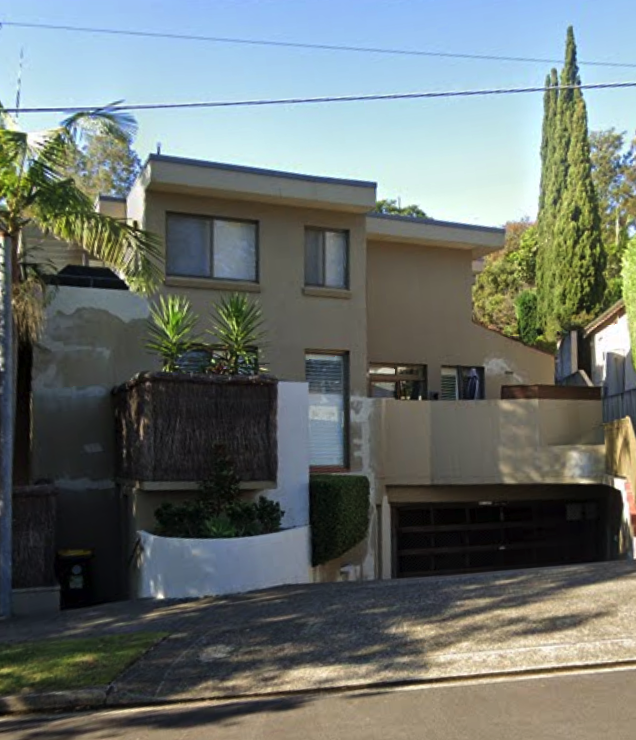 Modern beige multi-story house with large windows, a garage, and landscaped plants in a hilly neighborhood.
