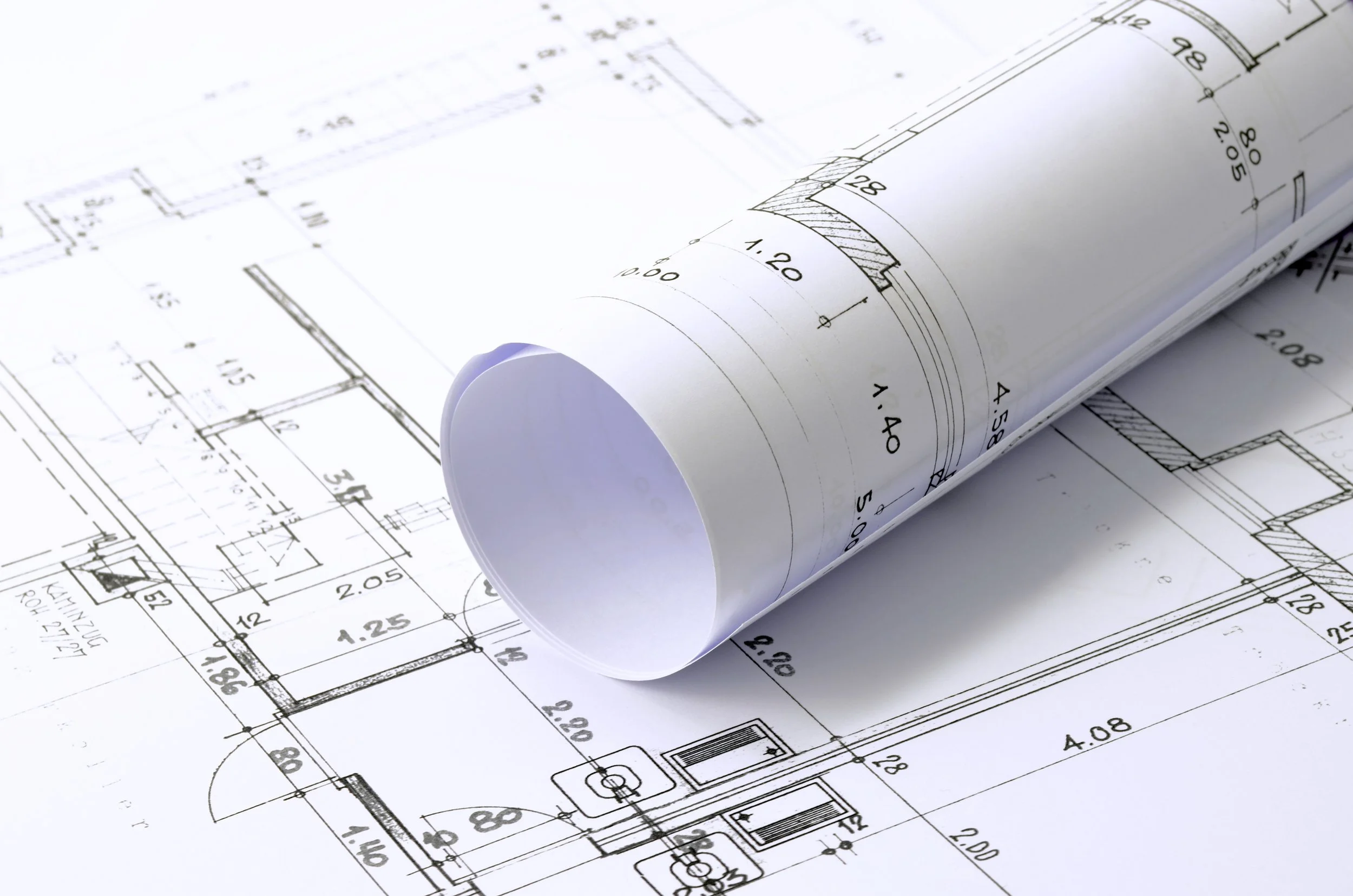 Rolled architectural blueprint on top of an unfolded blueprint, showing detailed layout and measurements.